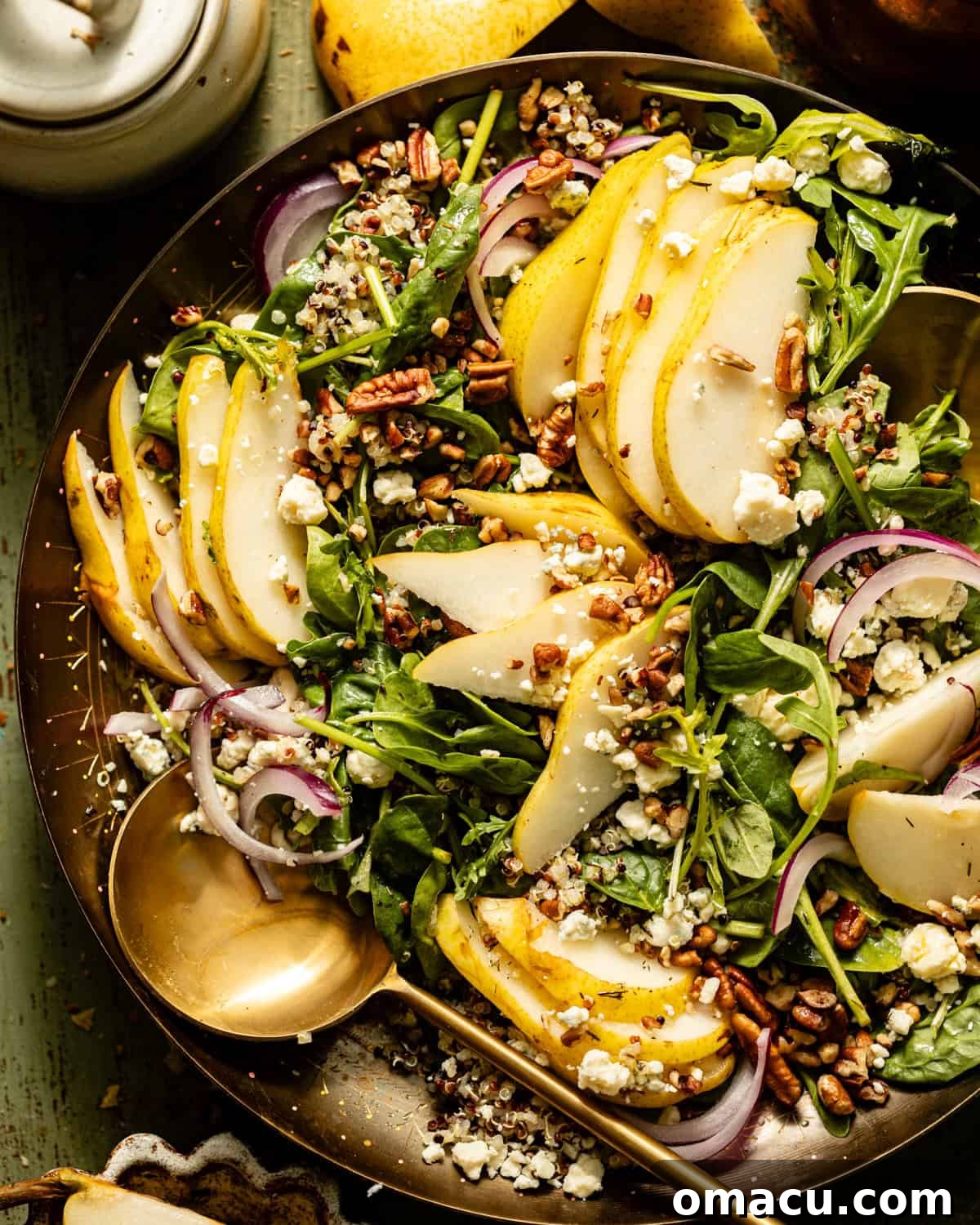 Arugula Pear Salad served in an elegant gold dish with serving spoons, accompanied by sliced pears on the side.