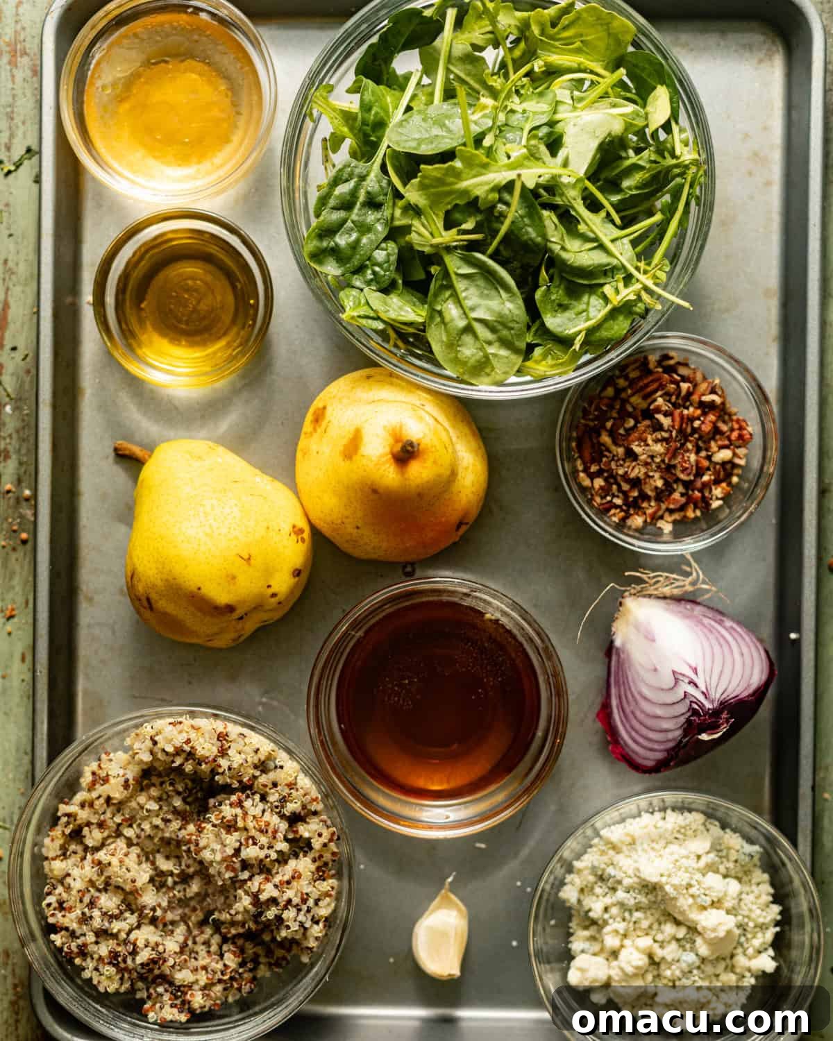 Ingredients laid out on a tray for Arugula Pear Salad: fresh arugula, cooked quinoa, ripe pears, red onion, walnuts, Gorgonzola cheese, maple syrup, lemon, garlic, and apple cider vinegar.
