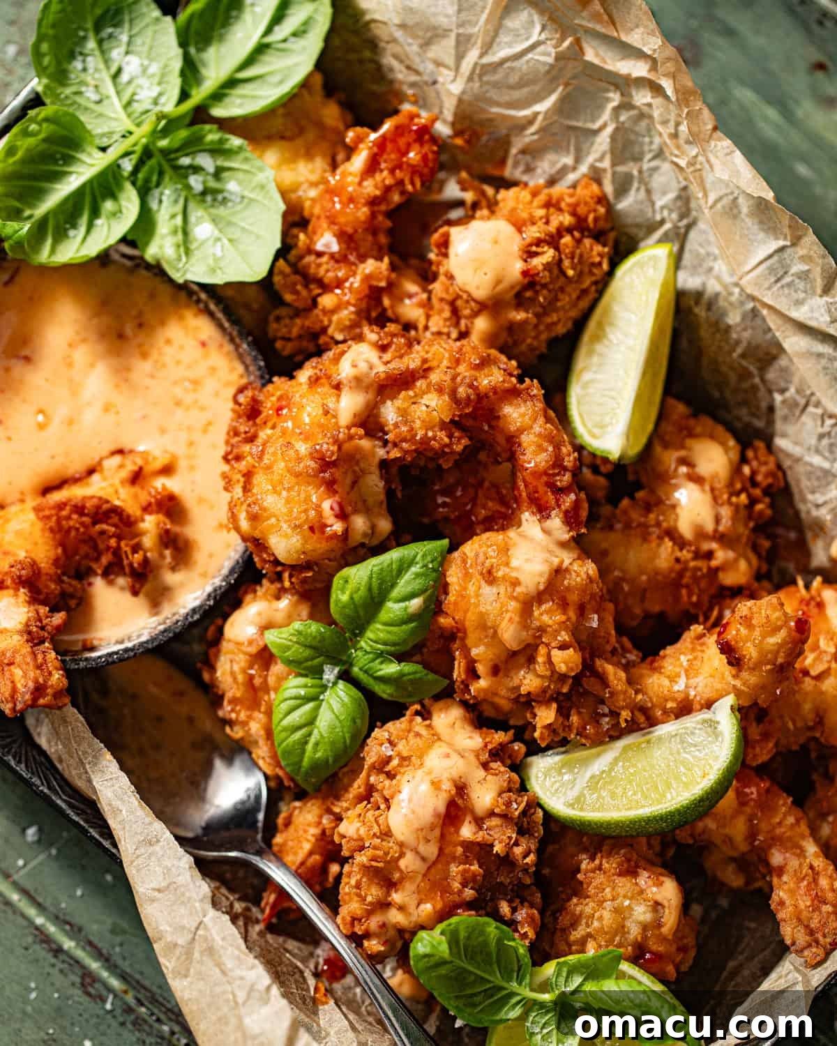 Crispy Bang Bang Shrimp served in a rustic basket, generously drizzled with Bang Bang sauce and garnished with fresh basil leaves, ready to be enjoyed.