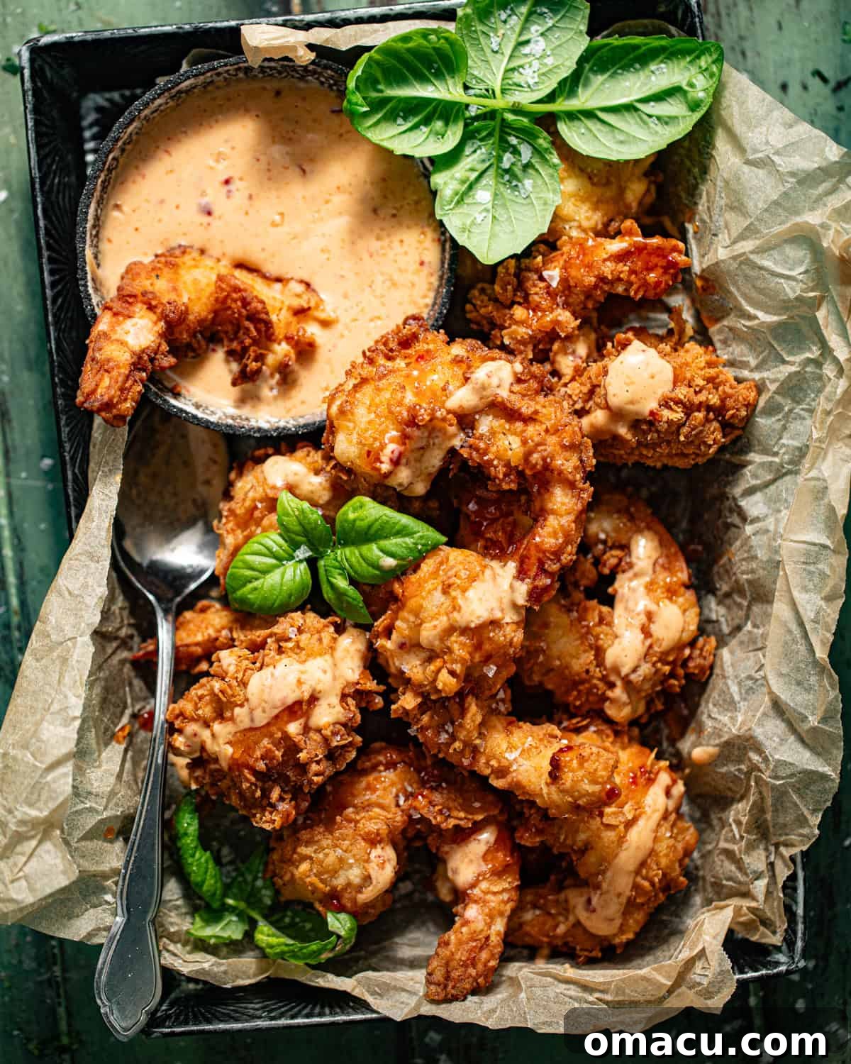 A generous serving of Bang Bang Shrimp in a bowl, lined with parchment paper, showcasing the beautiful golden crispness and creamy sauce.