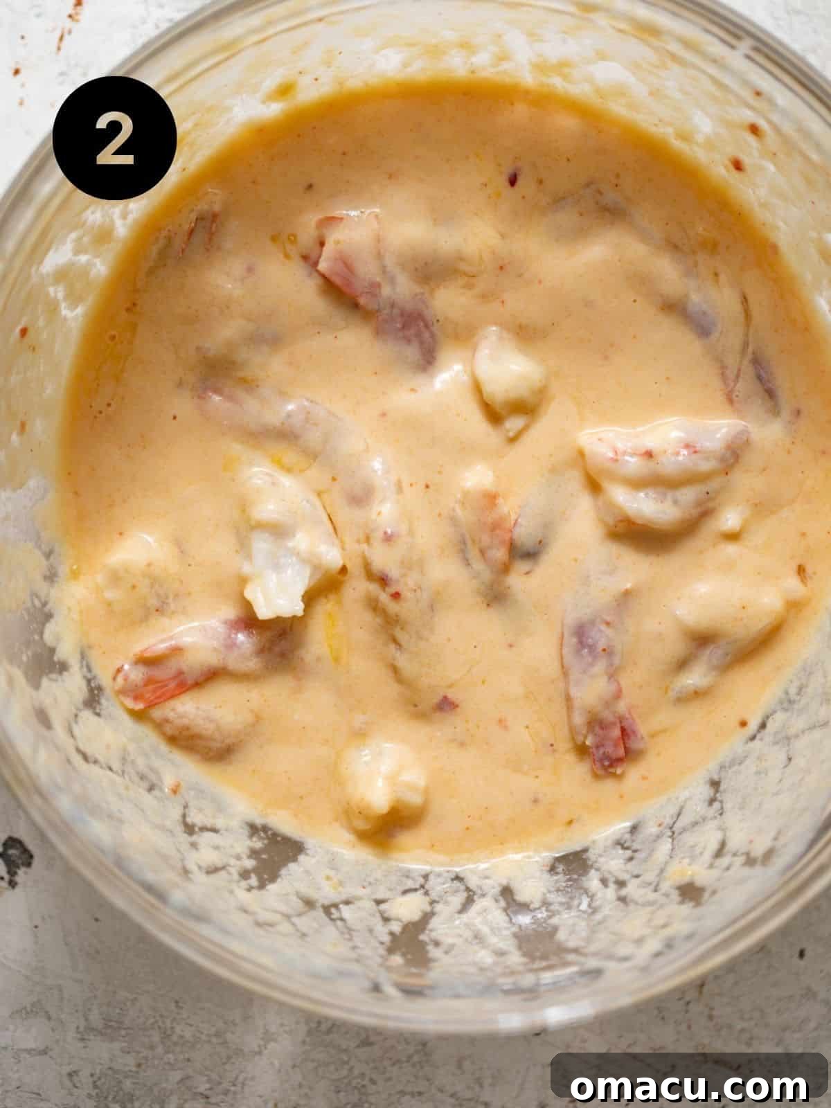 Raw shrimp submerged in a creamy buttermilk and egg mixture in a bowl, preparing them for the crispy coating.