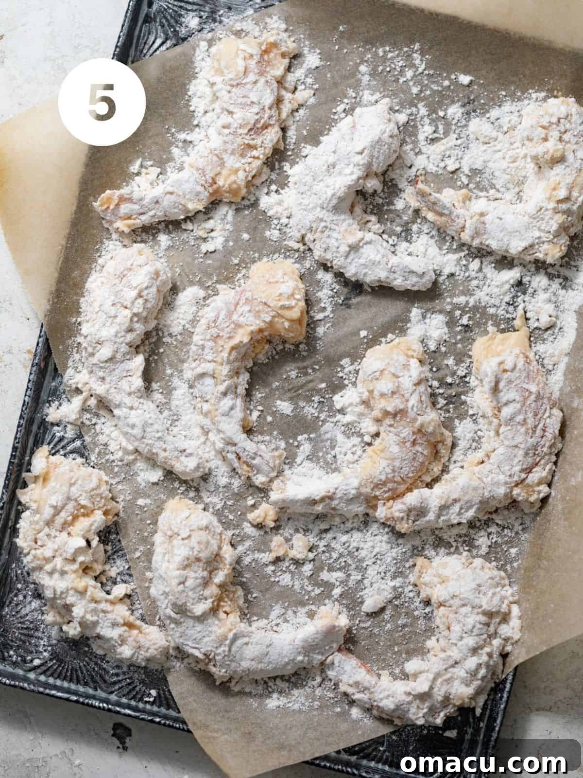 Fully coated shrimp laid out on a parchment-lined baking sheet, waiting to be fried, displaying their shaggy breading.