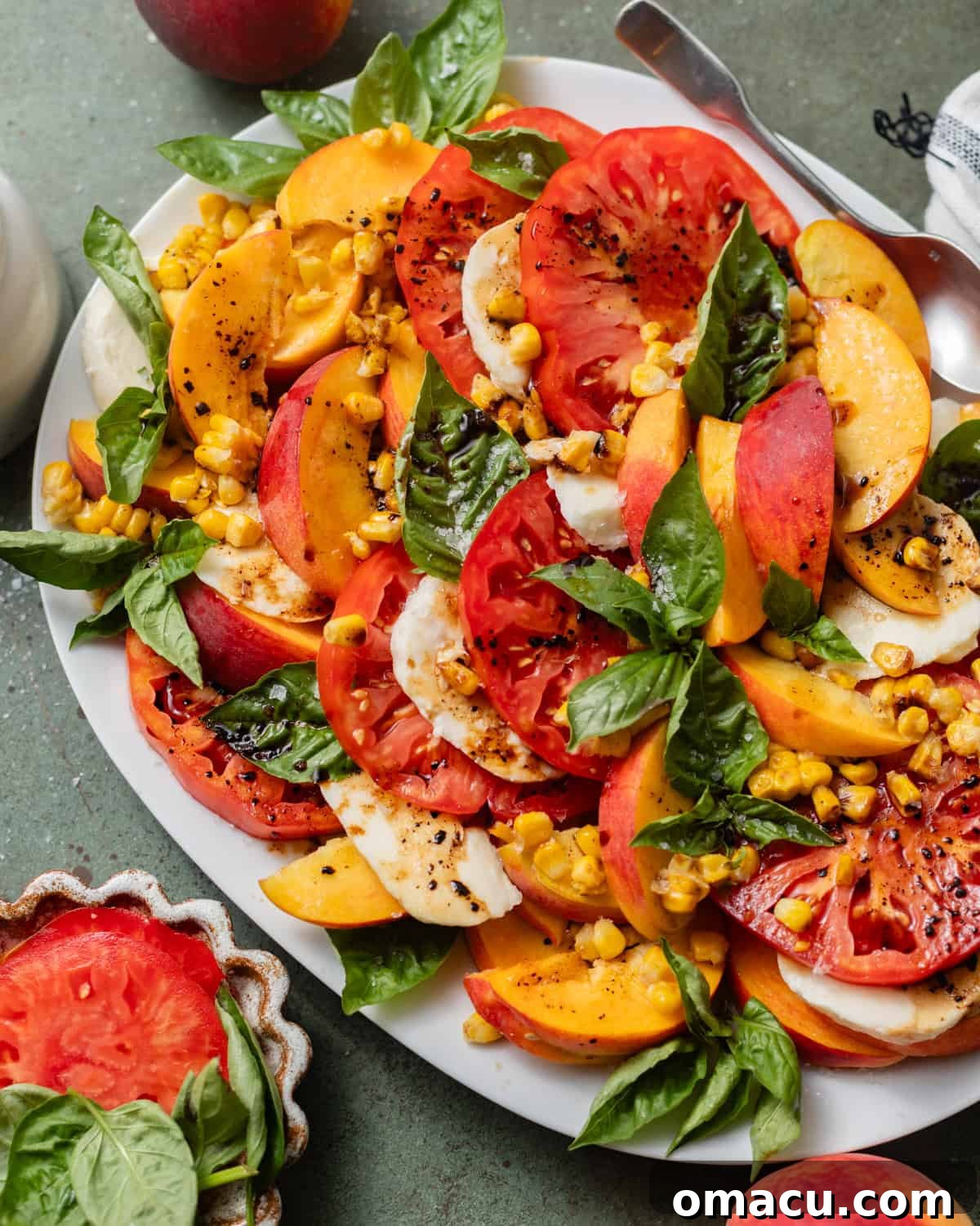 A beautifully assembled Peach Caprese Salad on a large white serving plate, with a generous drizzle of homemade balsamic glaze and a sprinkle of flaky sea salt, ready to be served.