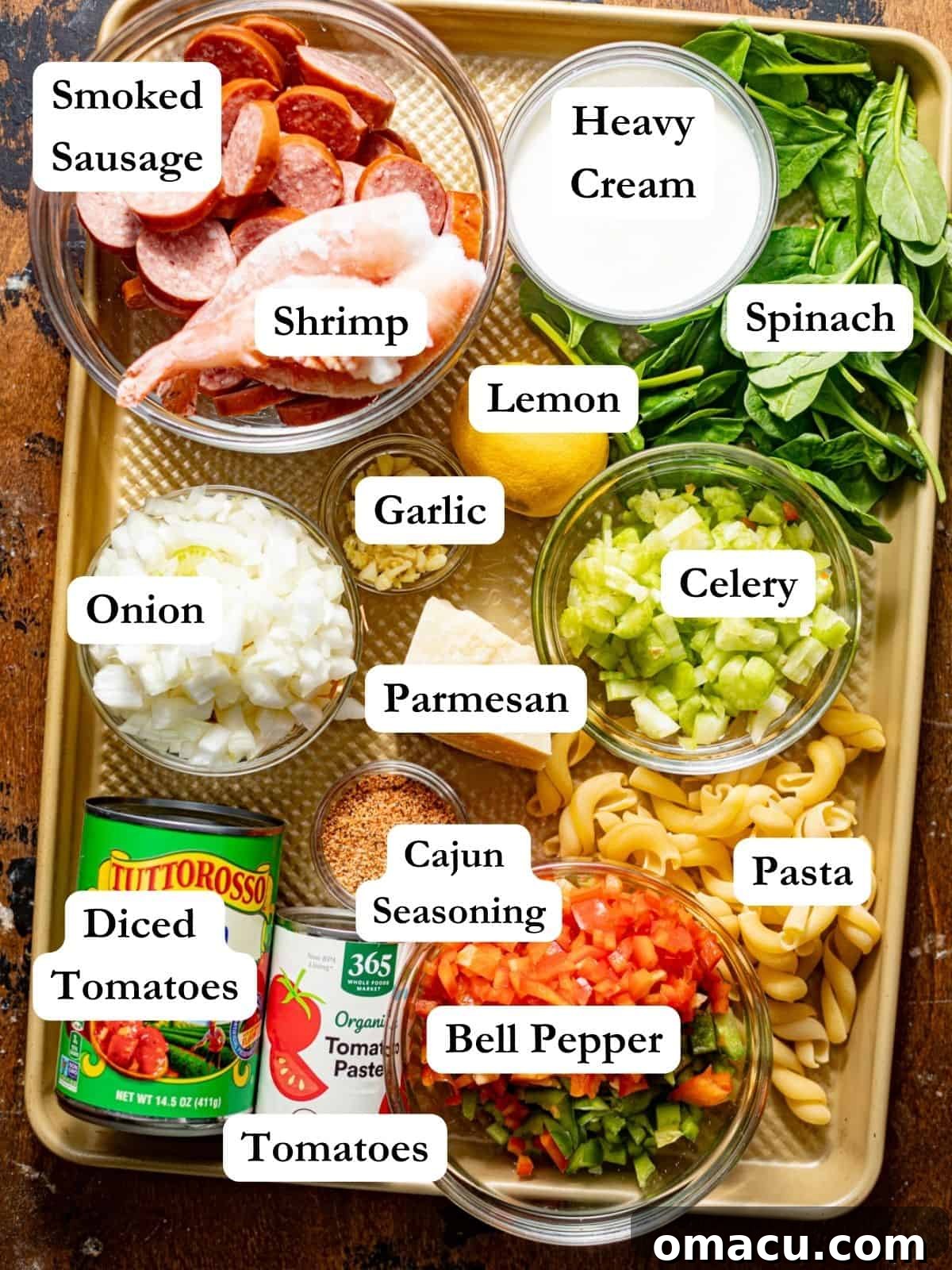 Individual ingredients laid out on a baking tray, including shrimp, sausage, bell peppers, celery, onion, and spices, for making Cajun shrimp and sausage pasta.