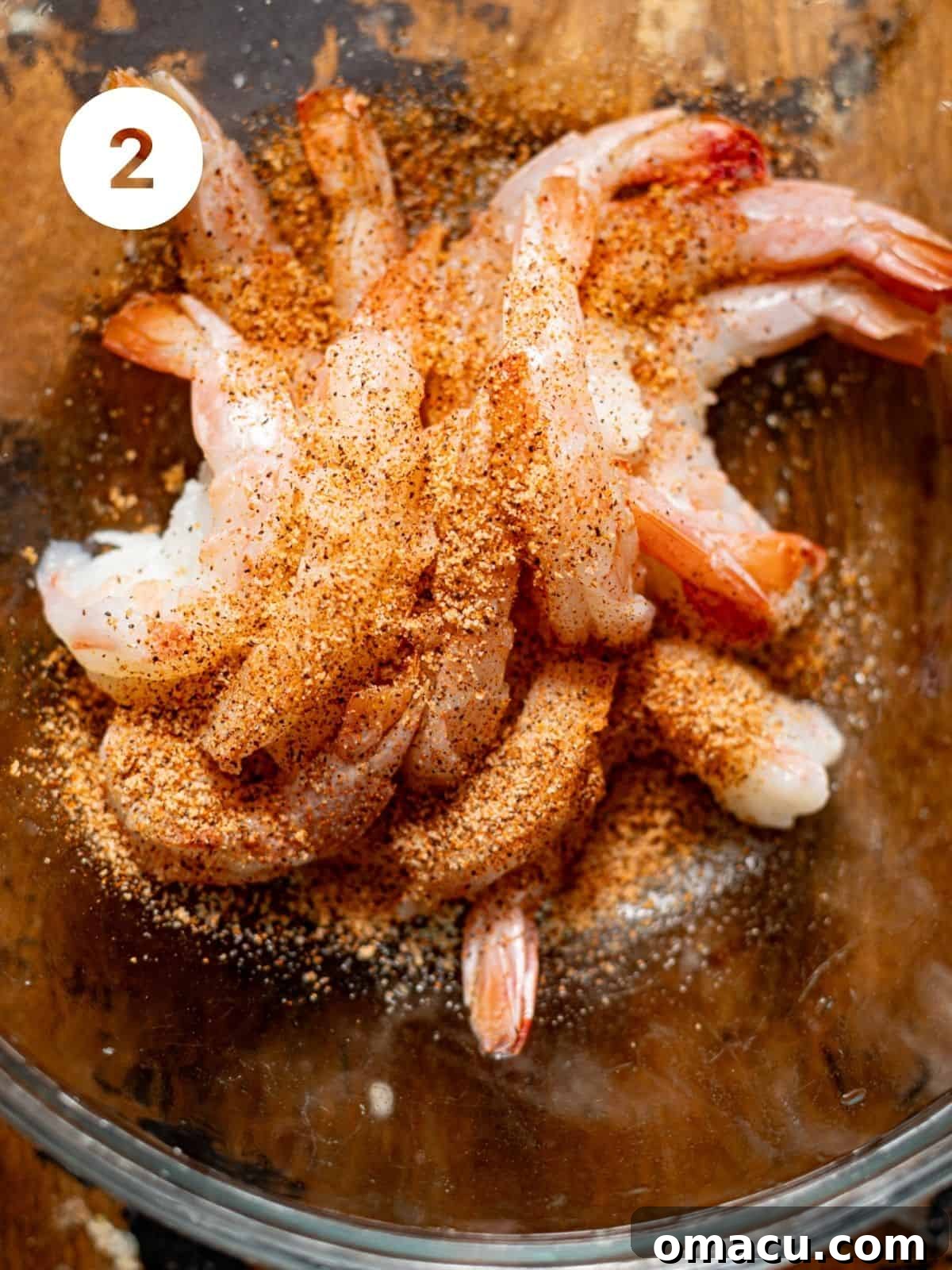 Raw shrimp seasoned with Cajun spices, salt, and pepper in a mixing bowl.