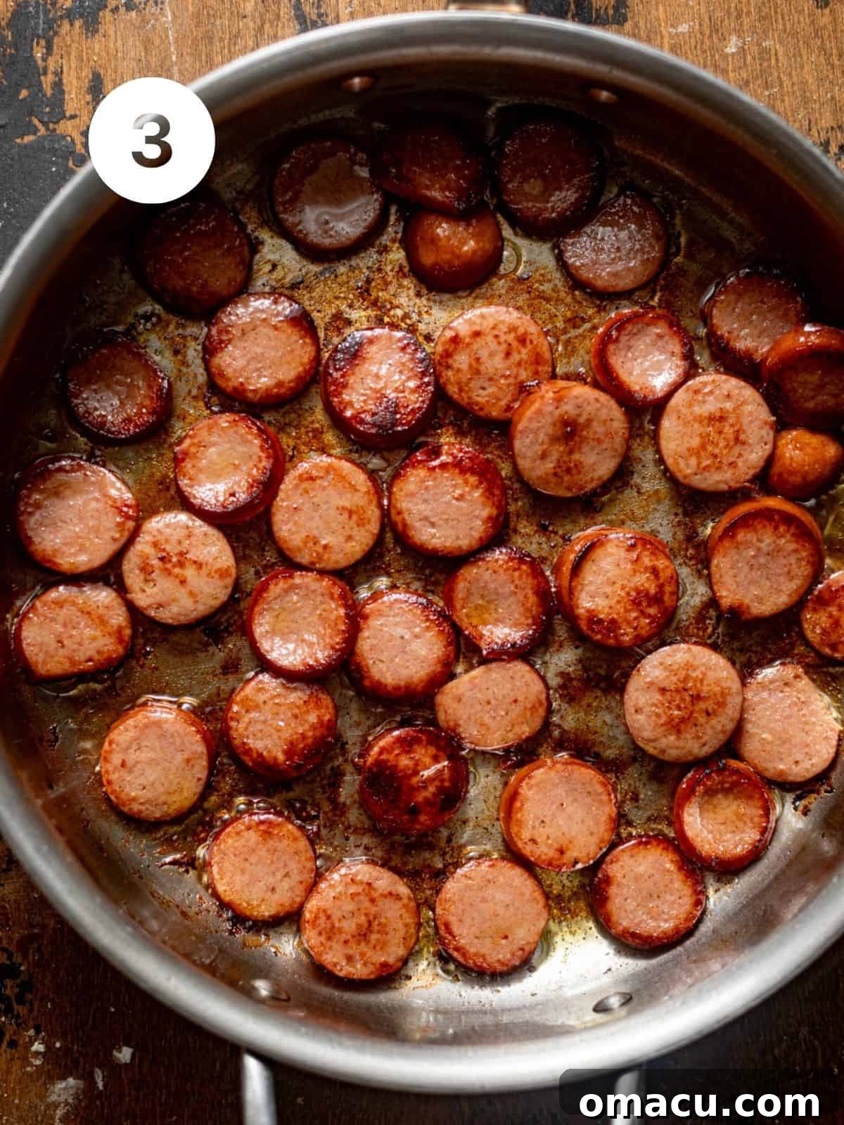 Sliced smoked Andouille sausage browning in a large skillet with olive oil.