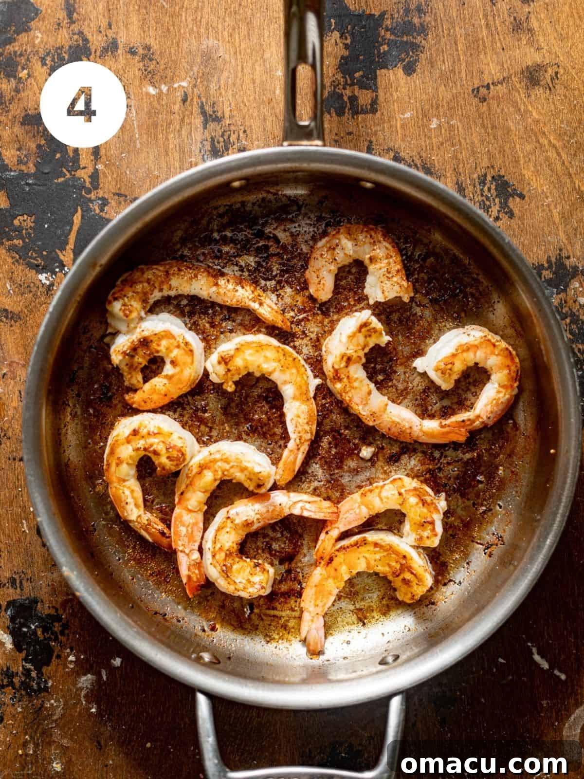 Pink, curled shrimp cooking in a skillet, absorbing the flavors left by the sausage.