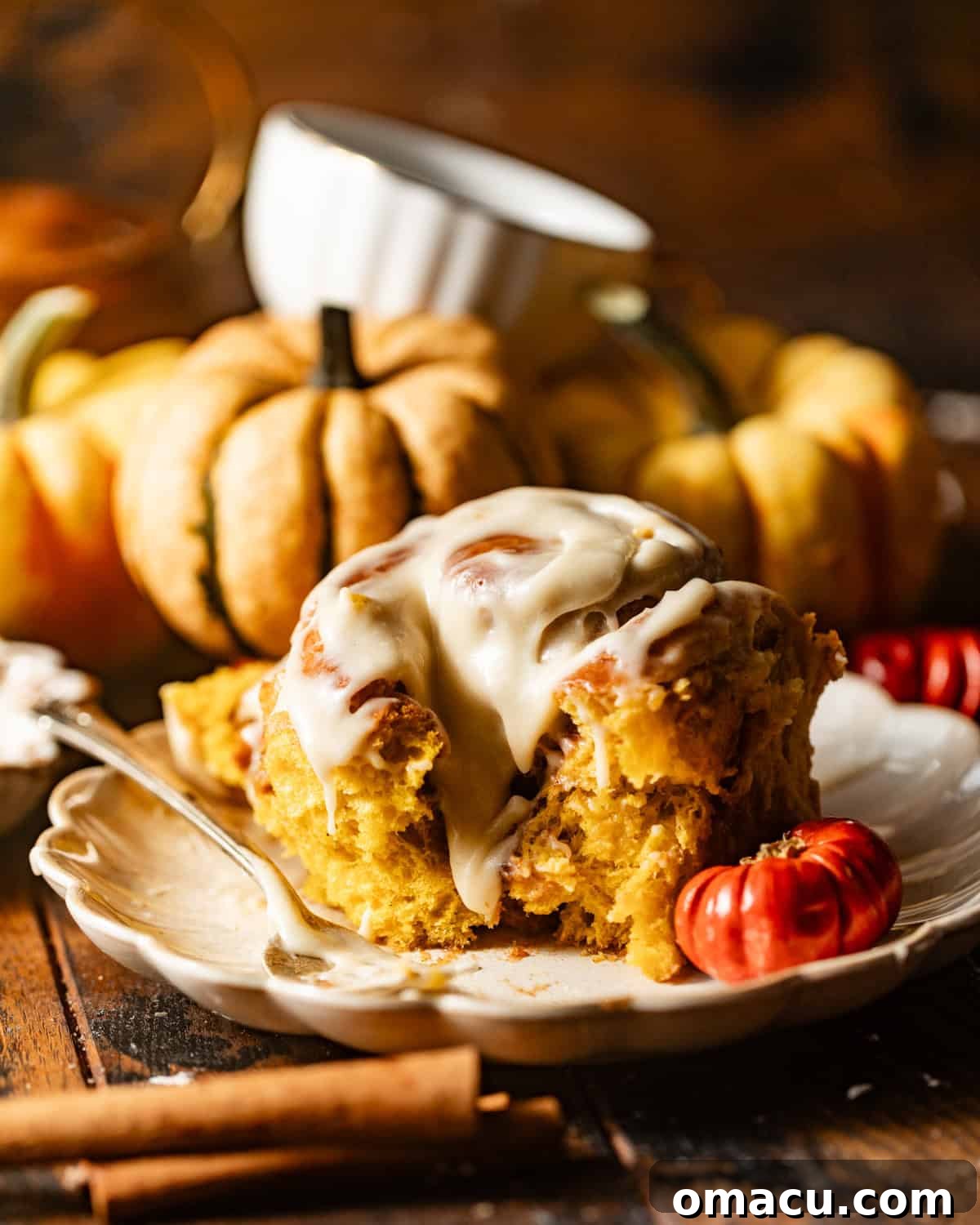A perfectly baked pumpkin cinnamon roll on a white plate, drizzled generously with maple glaze, surrounded by small decorative pumpkins and autumn leaves.