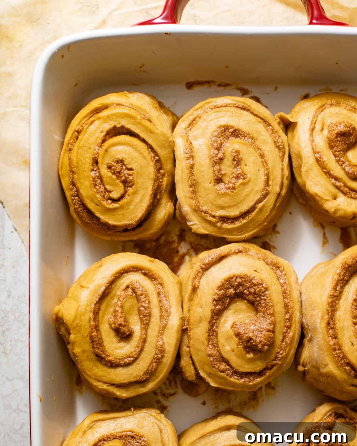 Pumpkin cinnamon rolls in the baking dish, covered with a kitchen towel for their second rise.