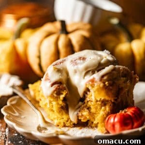 Close-up photo of a pumpkin cinnamon roll on a plate with maple glaze, garnished with cinnamon sticks.