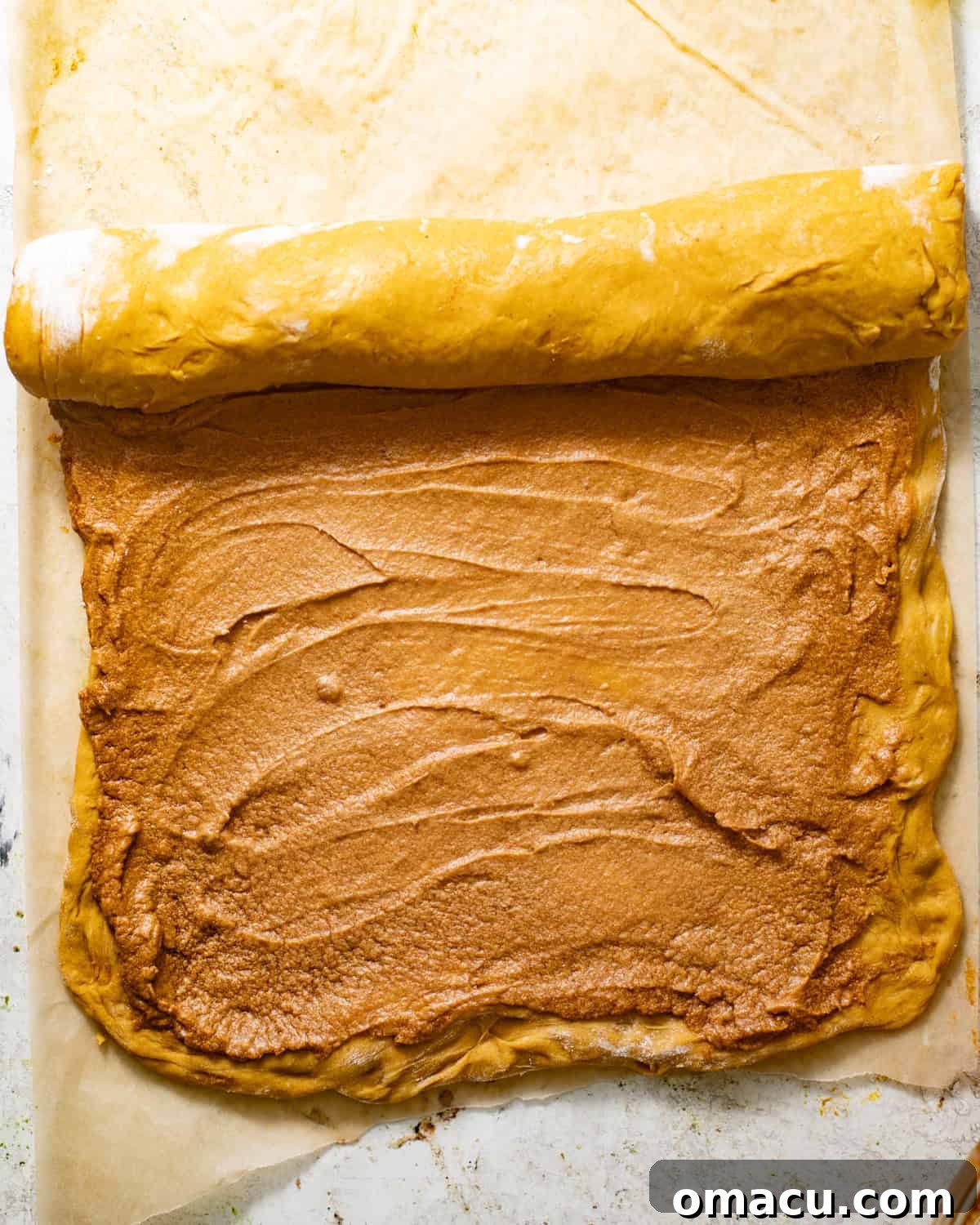 Pumpkin cinnamon roll dough tightly rolled into a log, ready for slicing.