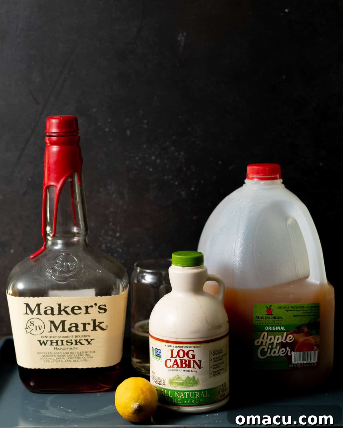 All the ingredients needed to make an apple cider bourbon cocktail, including whiskey bourbon, maple syrup, apple cider, lemon juice, and ginger beer.