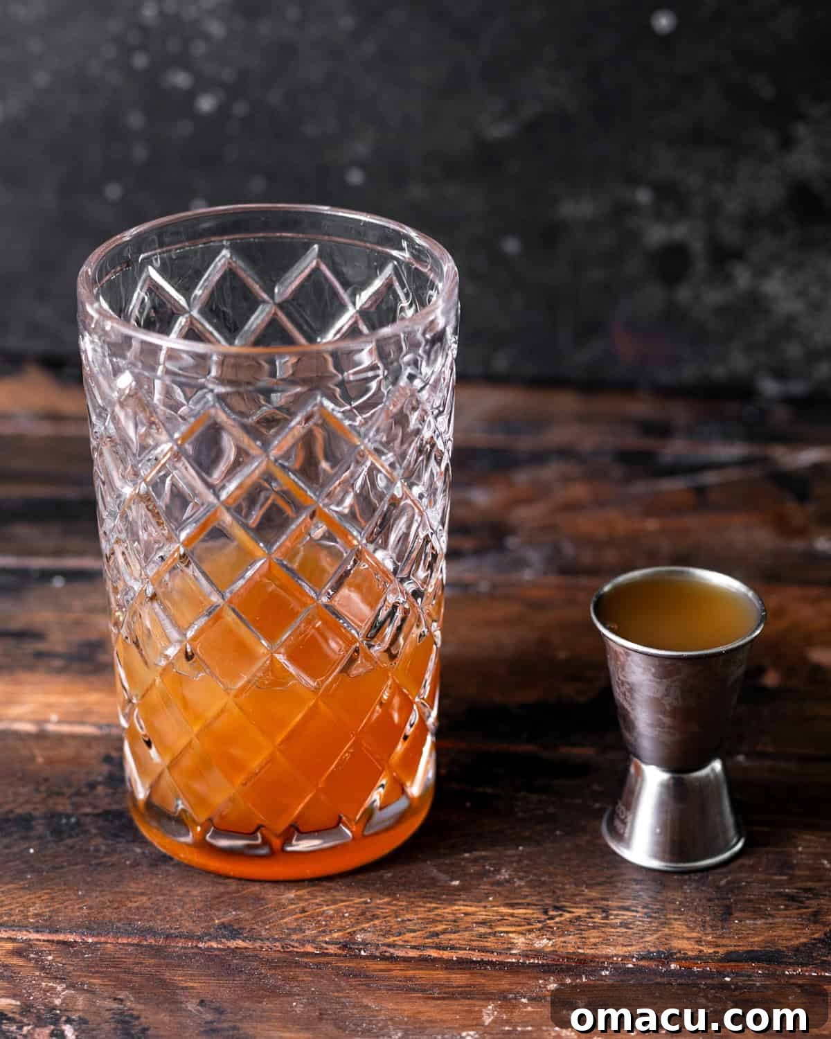 Apple cider, whiskey, lemon juice, maple syrup, and cinnamon measured into a cocktail shaker with a jigger next to it.