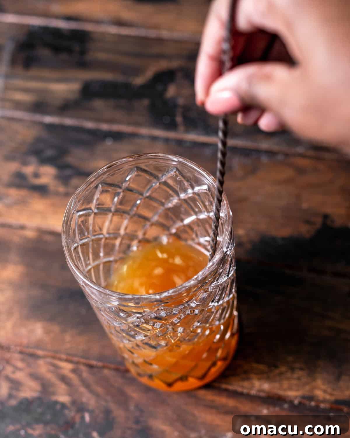 A hand stirring the apple cider cocktail together in a cocktail shaker with a spoon.