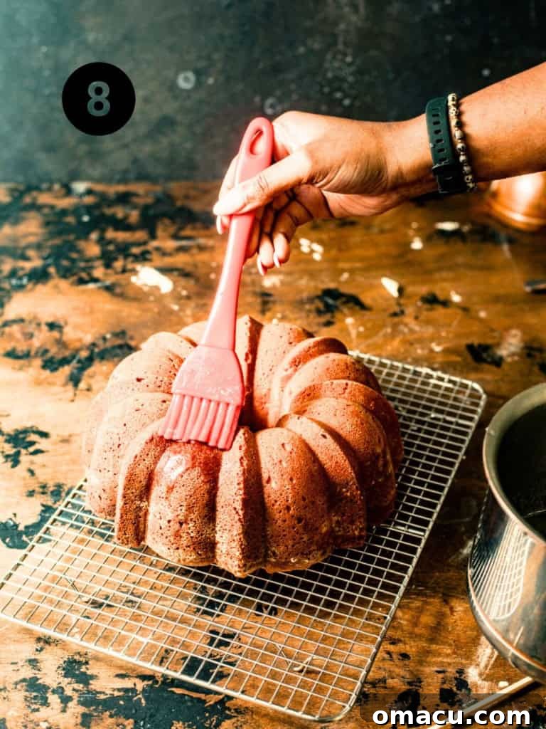 The pound cake being brushed with the remaining lemon simple syrup after being unmolded onto a cooling rack.