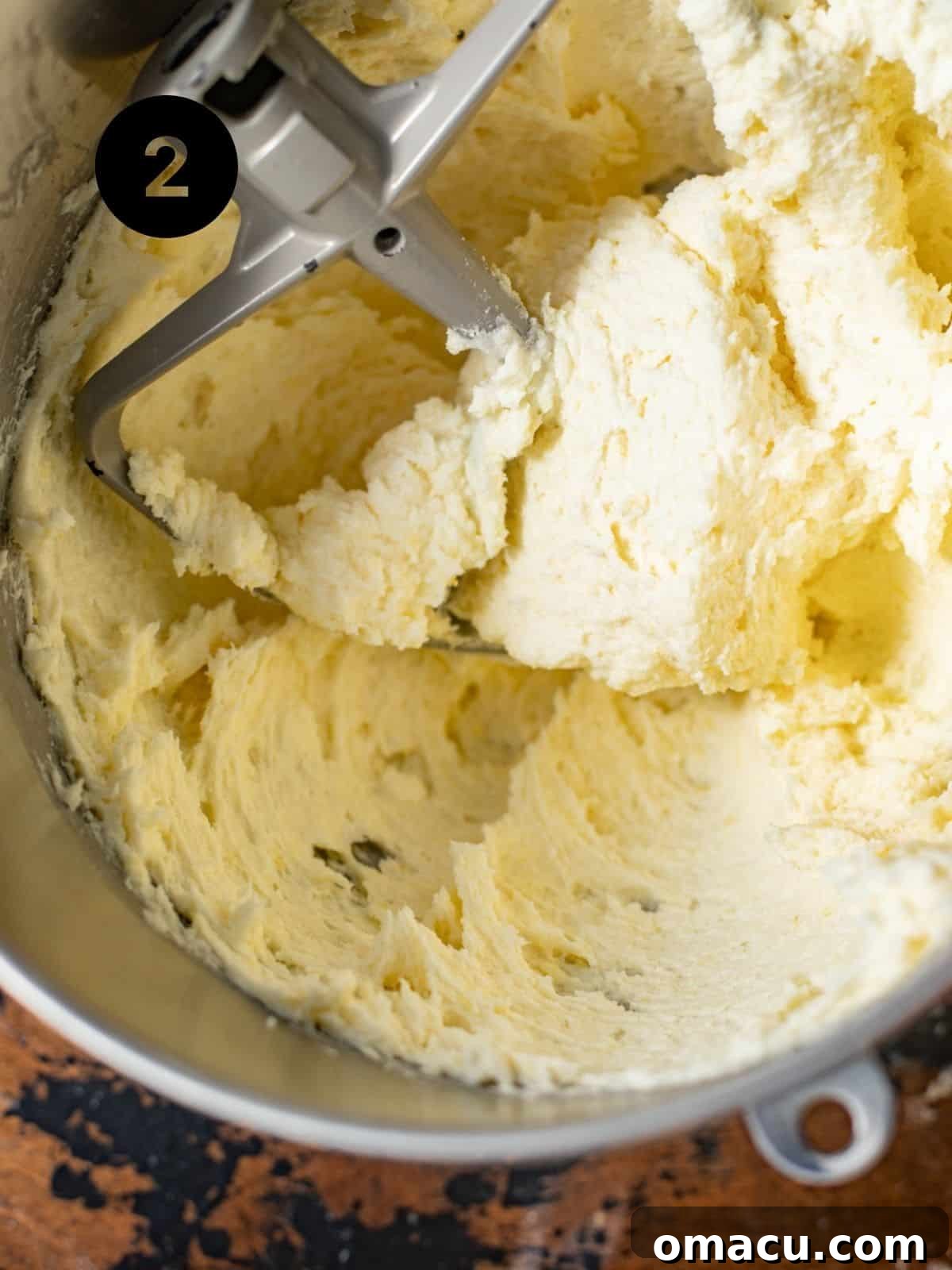 Butter, sugar, and cream cheese being creamed together in a metal mixing bowl, achieving a light and fluffy consistency.