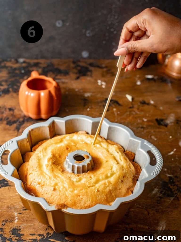 A toothpick being used to poke holes into the lemon cream cheese pound cake while still in the bundt pan, preparing it for the syrup.