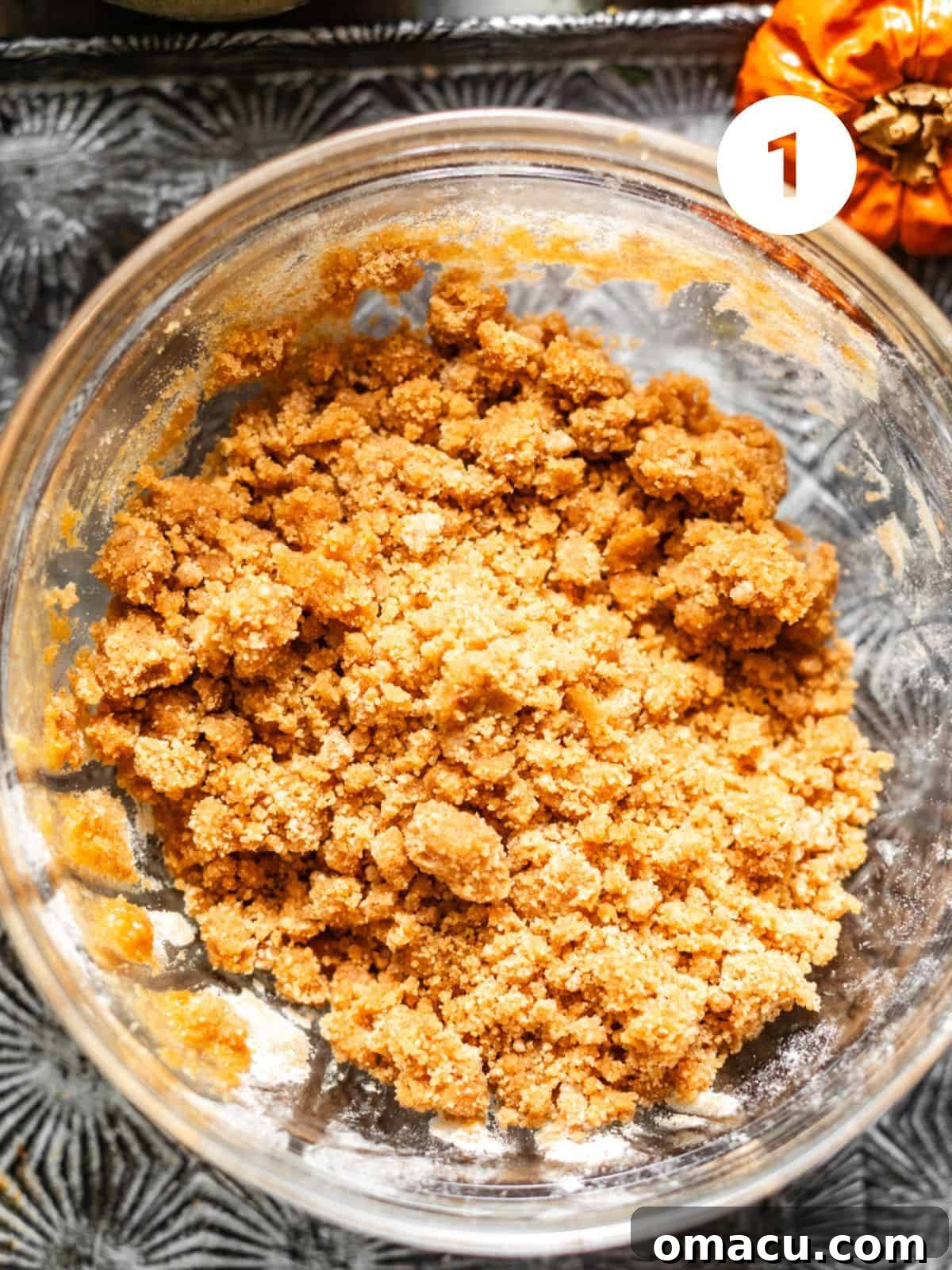 A glass mixing bowl holds the prepared cinnamon streusel topping, a perfect crumble of brown sugar, all-purpose flour, cinnamon, and melted butter, ready to be chilled.