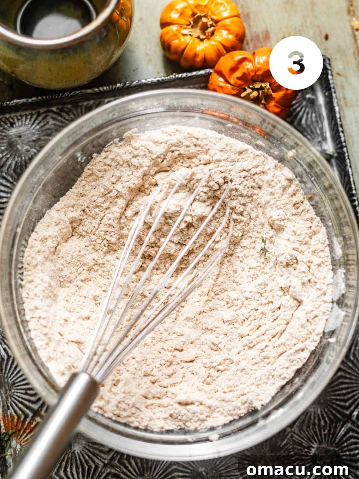 A bowl of expertly combined dry ingredients for the pumpkin muffins, including flour, baking powder, baking soda, and a delightful blend of warm spices, all whisked together for even distribution.