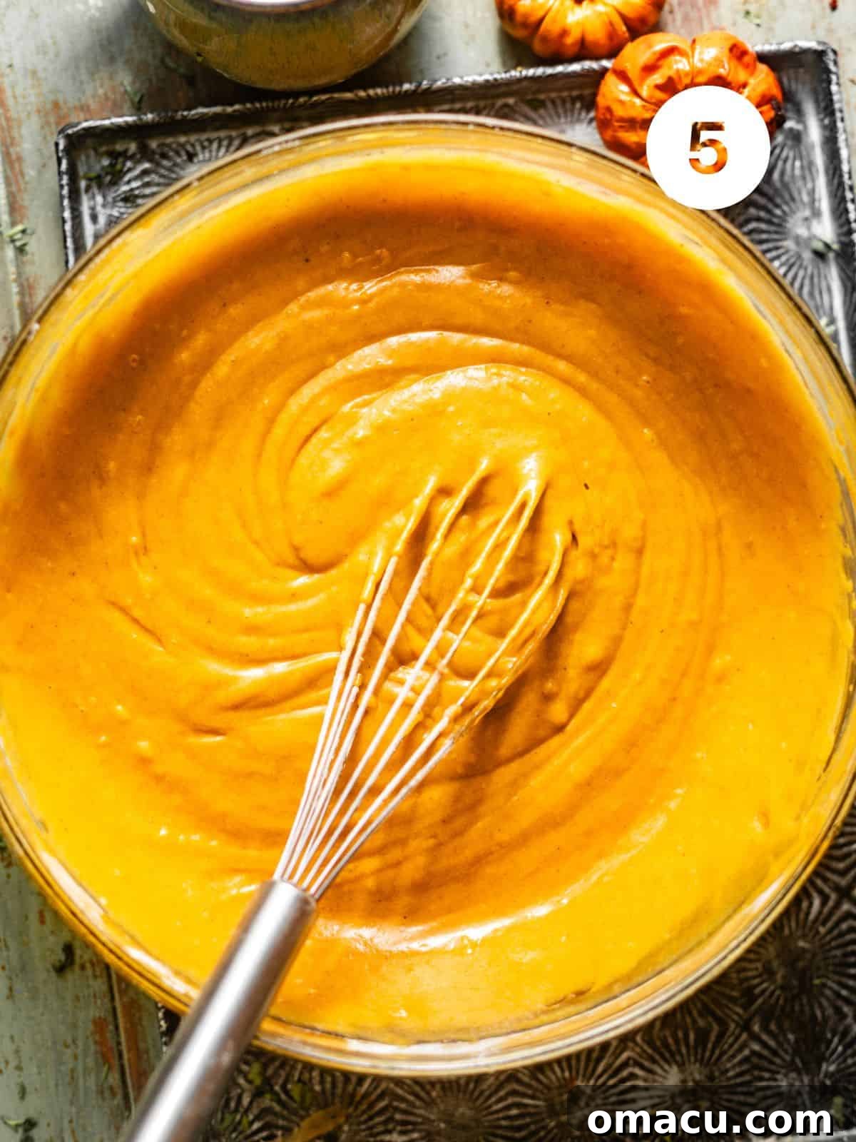 The pumpkin muffin batter, light and airy, rests in a mixing bowl after the wet and dry ingredients have been gently combined, showcasing a smooth and well-incorporated consistency ready for baking.