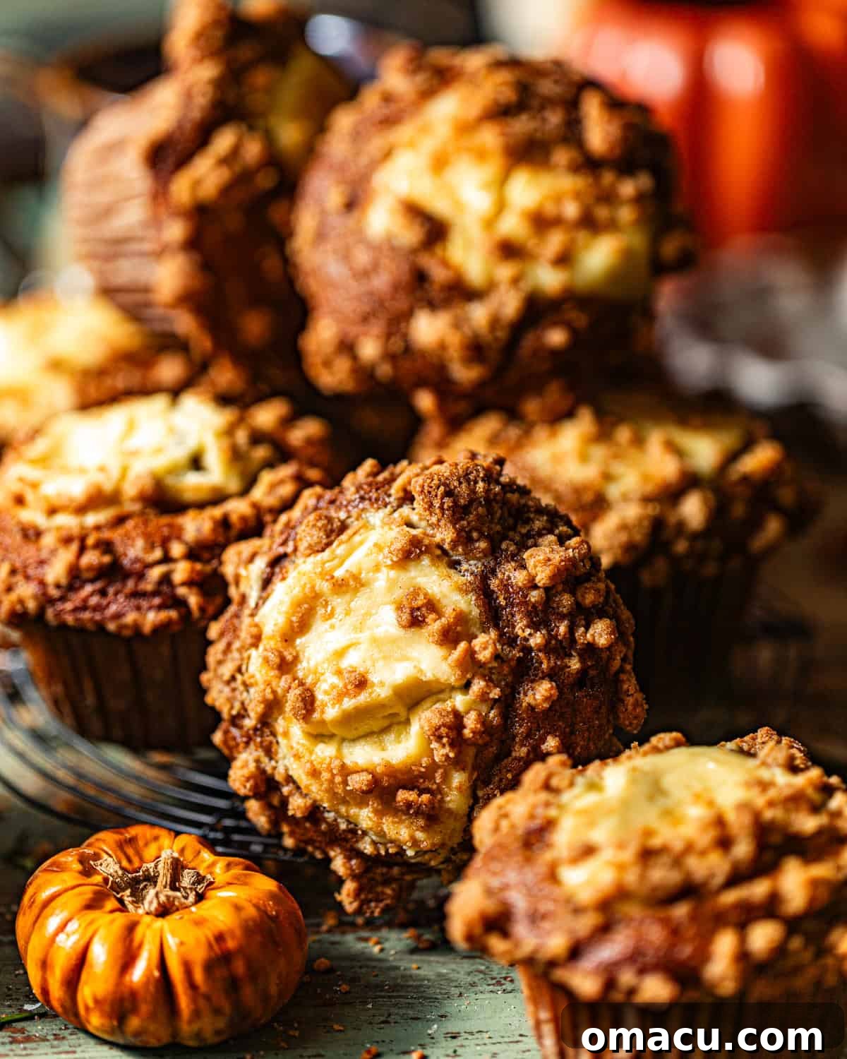 A stunning close-up photo of warm, golden-brown pumpkin cream cheese muffins resting on a wire cooling rack, highlighting their irresistibly fluffy texture, generous cream cheese swirl, and crunchy cinnamon streusel topping.