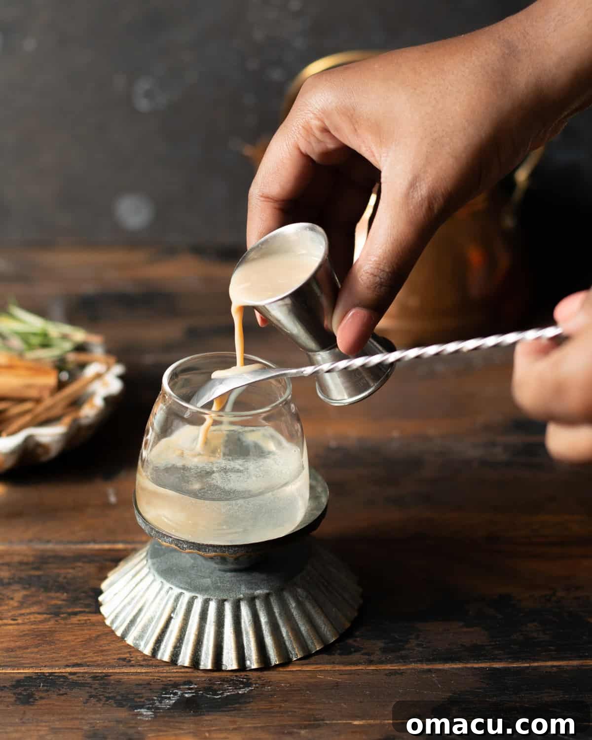 a hand pouring irish cream onto the back of a spoon and into the shot glass.