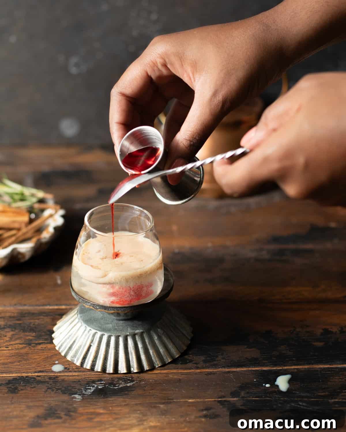 a hand pouring grenadine into a shot glass.