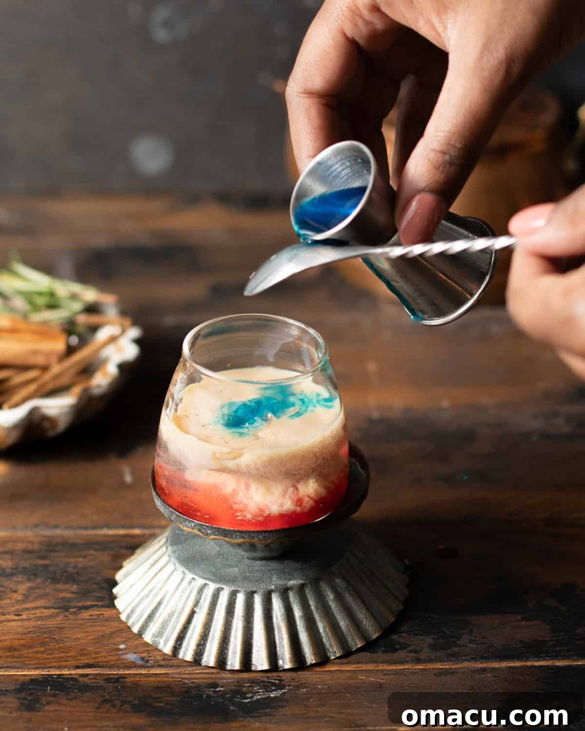blue curacao being poured onto the back of a spoon and into the shot glass.