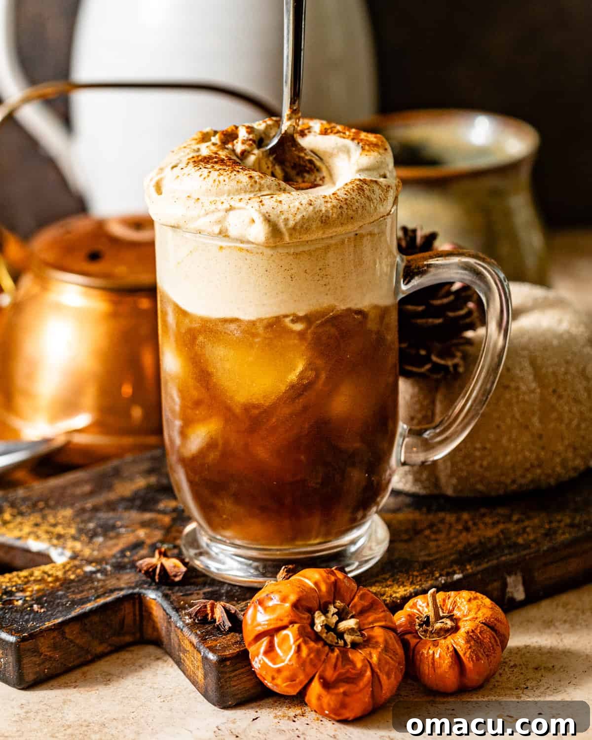 A glass of iced cold brew coffee topped with a thick layer of creamy pumpkin cold foam, being stirred gently with a spoon. The lighting is warm and inviting, suggesting a cozy autumn morning.