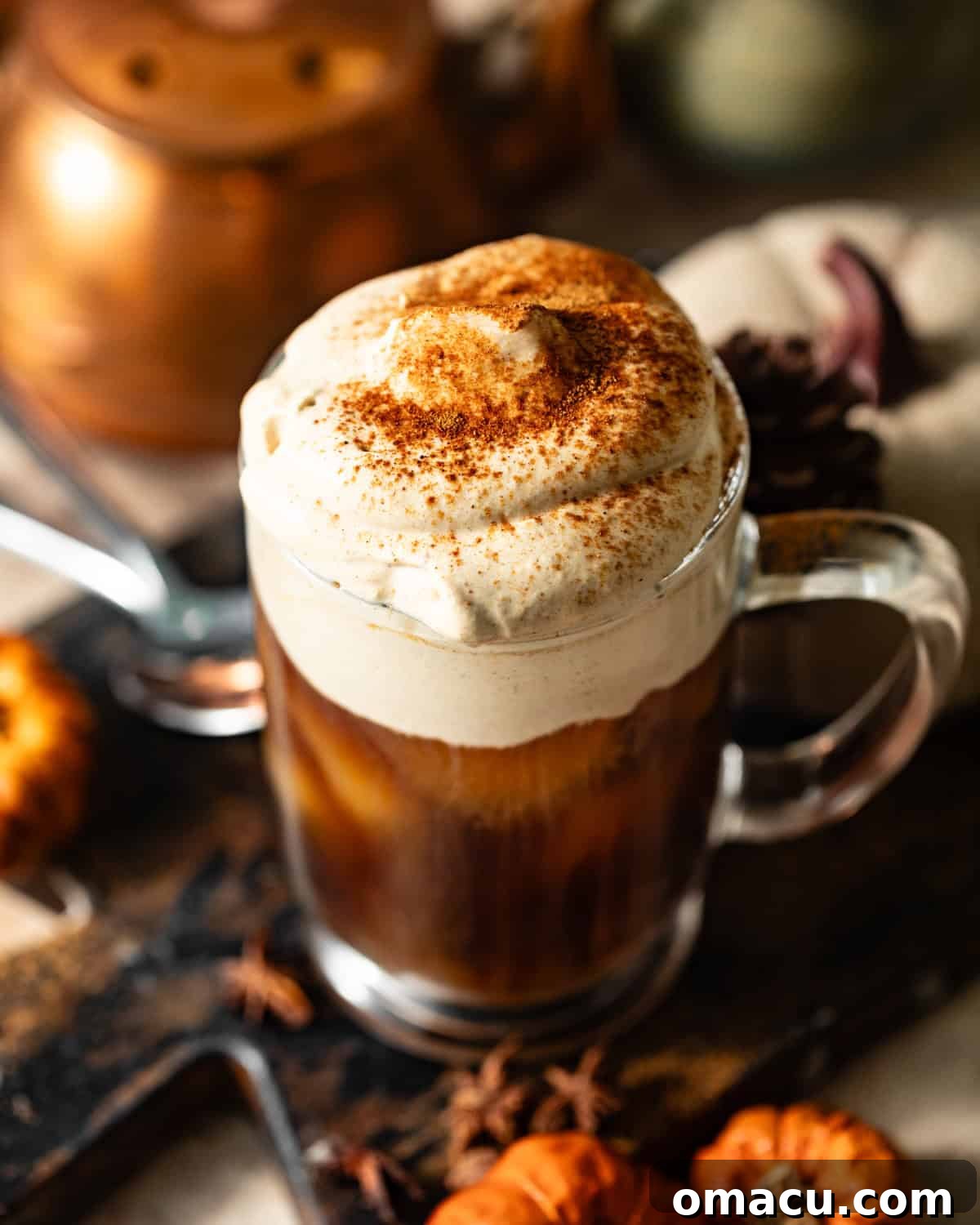 A close-up shot of rich, orange pumpkin cold foam resting in a clear glass, showing its creamy, airy texture. The foam looks light and inviting.
