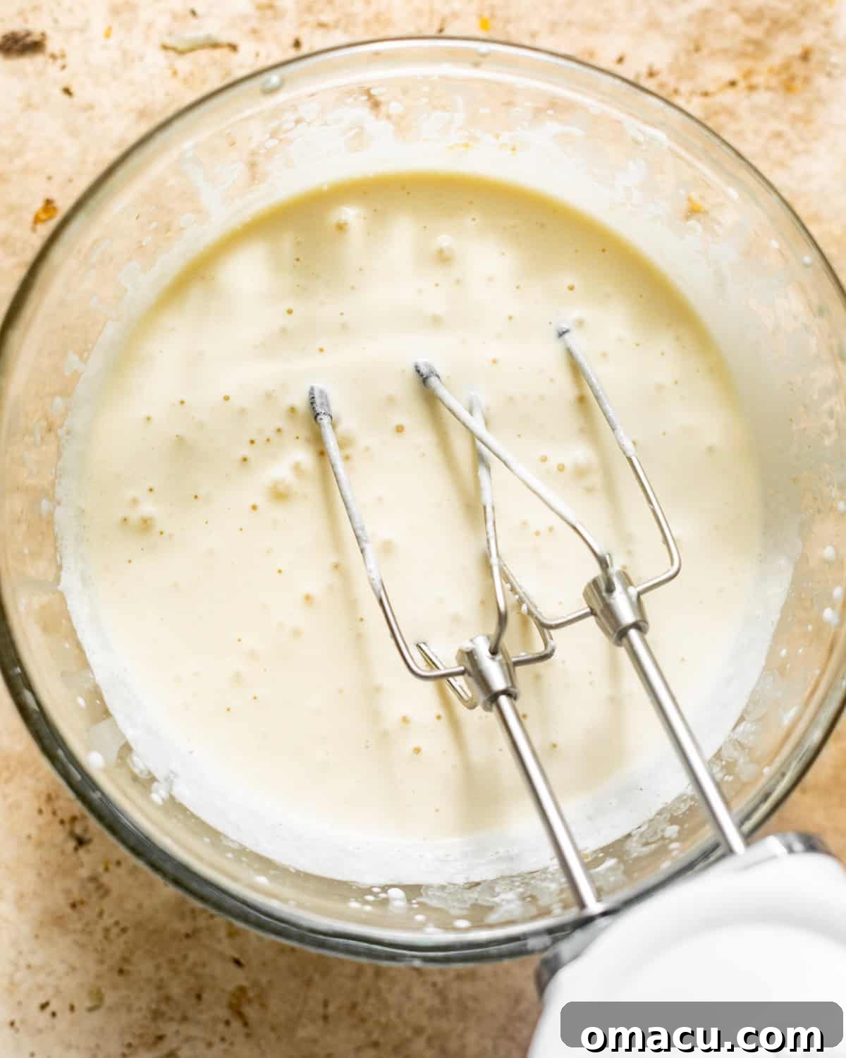 A mixing bowl containing heavy cream and brown sugar, with an electric hand mixer poised to begin whisking. The ingredients are perfectly prepped for the first step.