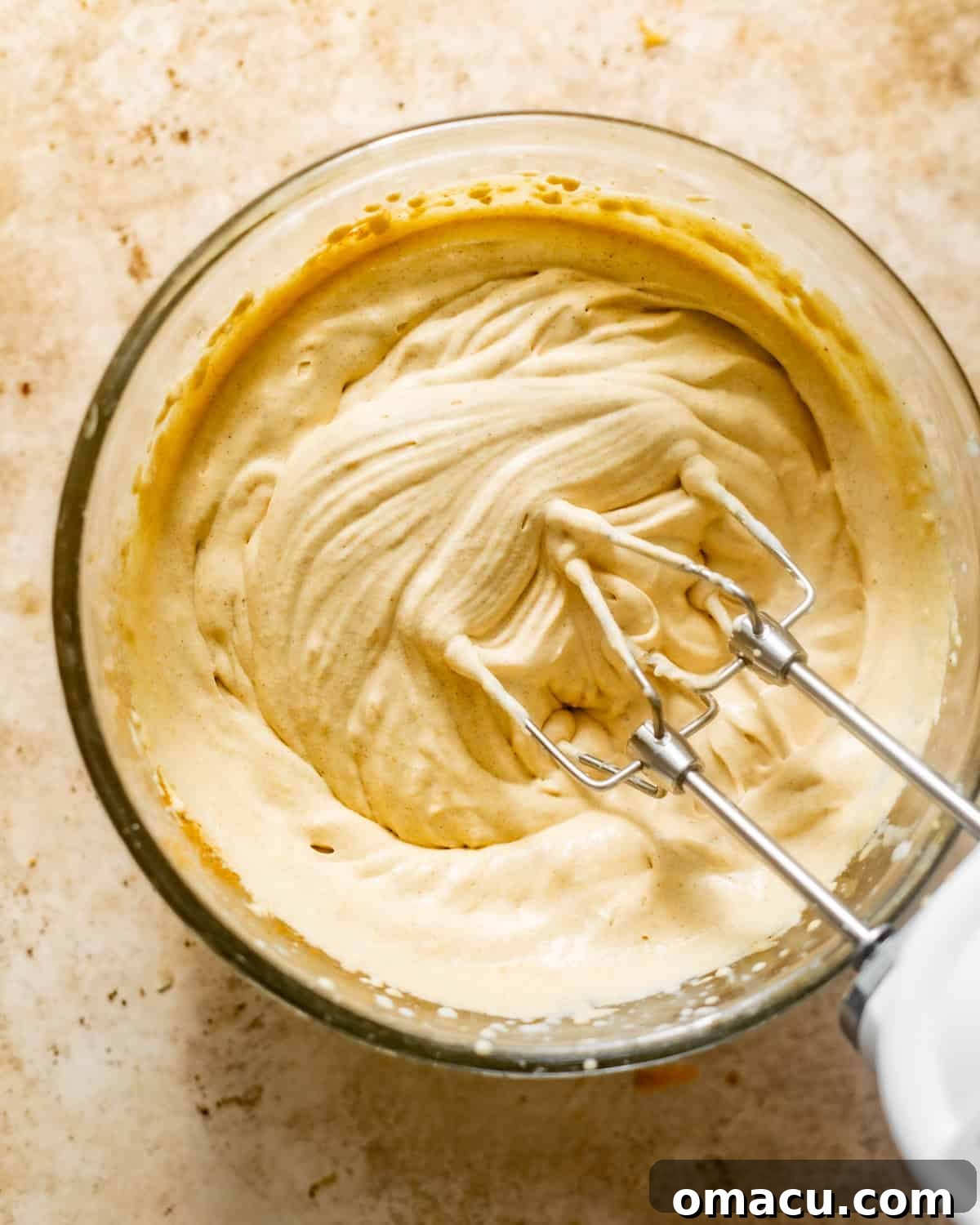 A bowl of pumpkin cold foam, fully mixed and fluffy, with an electric hand mixer showing its rich, creamy texture and warm orange hue.
