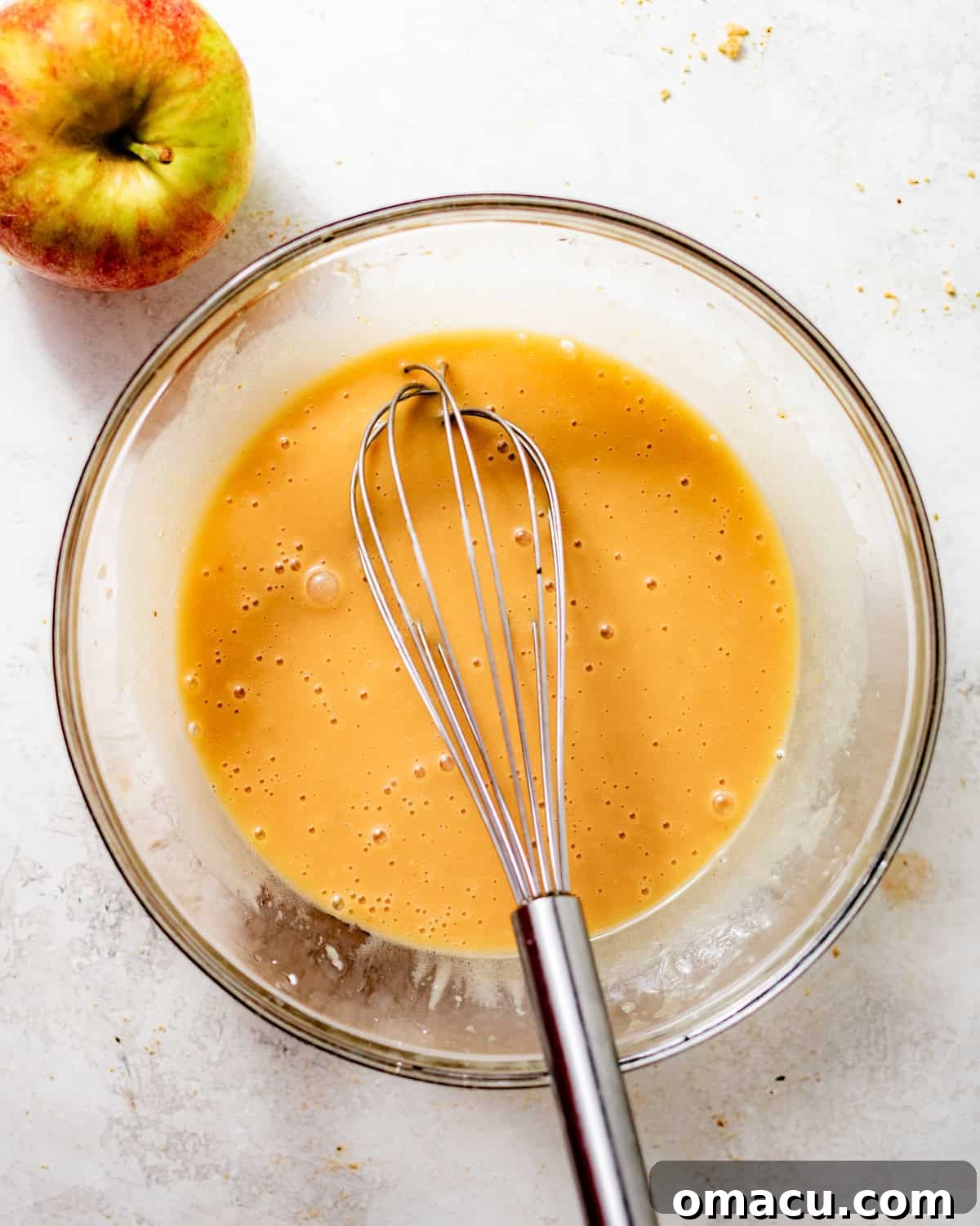 Wet ingredients for apple cider cupcakes, including reduced apple cider, eggs, sour cream, and vanilla extract, perfectly mixed in a separate bowl.
