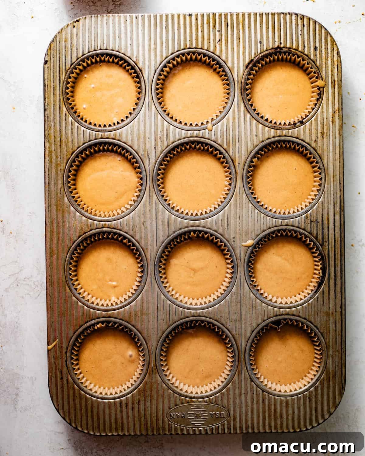 Apple cider cupcake batter carefully poured into lined muffin cups in a baking pan, ready to go into the oven.