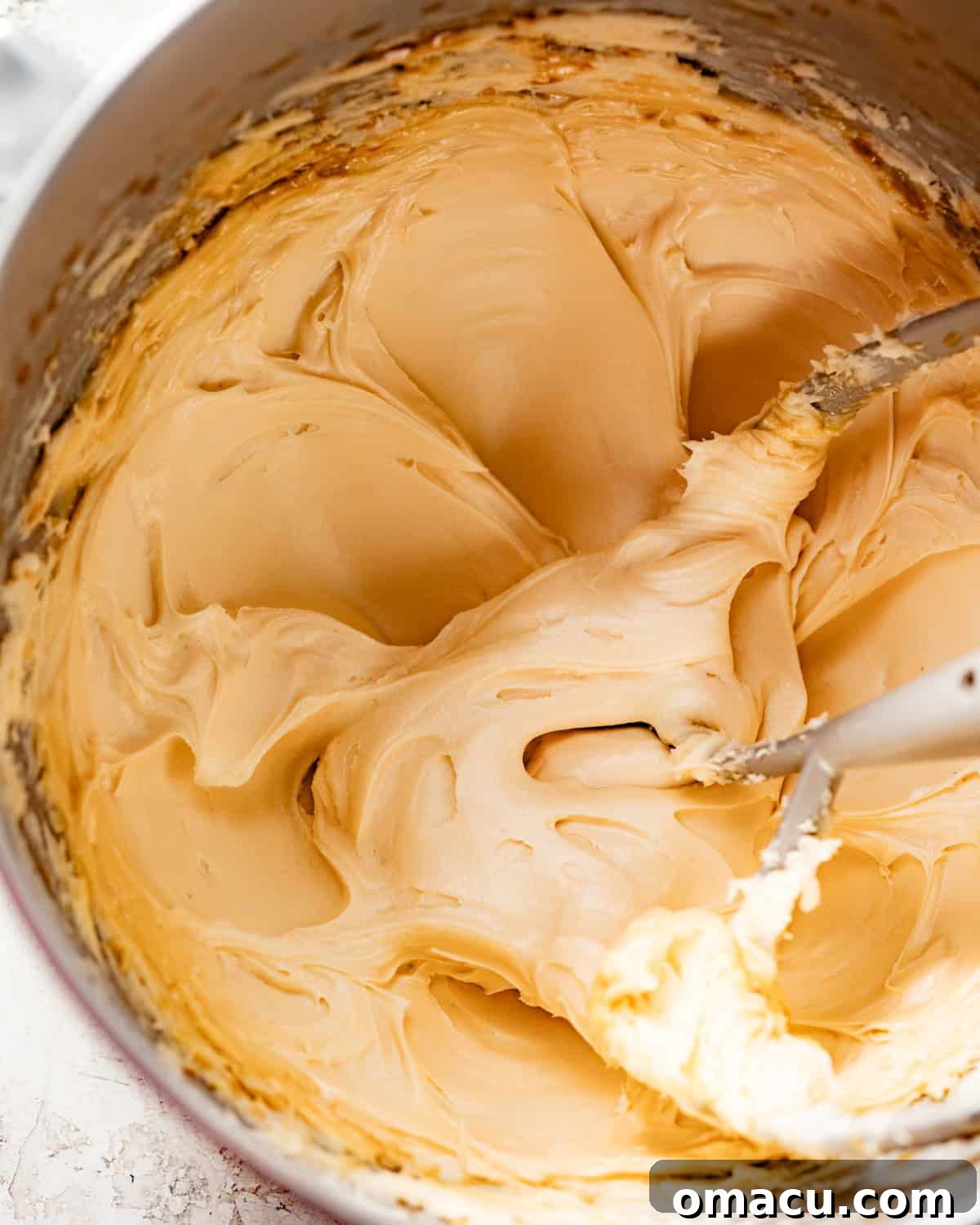 Smooth cinnamon cream cheese frosting being prepared in a stand mixer bowl with a paddle attachment.