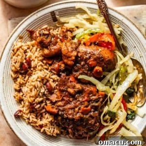 A delicious serving of brown stew chicken, accompanied by fluffy rice and peas and tender steamed cabbage on a plate.