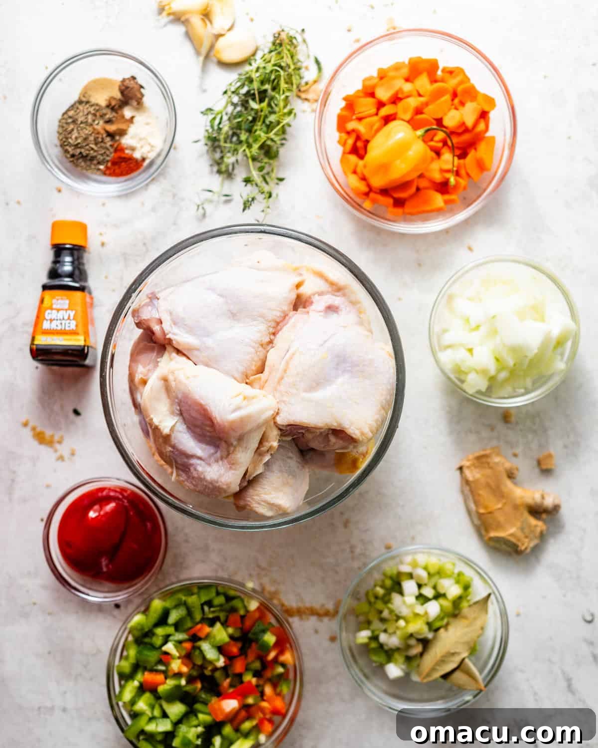 A vibrant array of fresh ingredients for brown stew chicken, including colorful bell peppers, aromatic herbs, and spices, laid out on a white surface.
