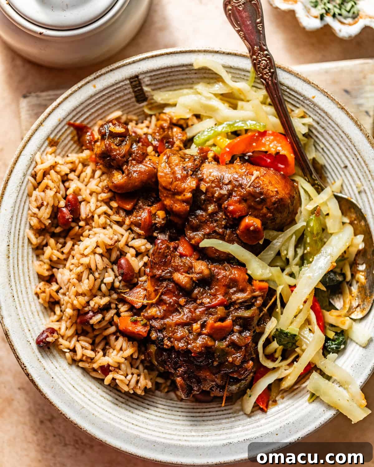 A hearty plate of Jamaican brown stew chicken, served alongside fluffy rice and peas and tender steamed cabbage, creating a complete and authentic Caribbean meal.
