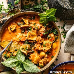 A steaming bowl of Tuscan tortellini soup, garnished with fresh basil leaves and grated Parmesan cheese.