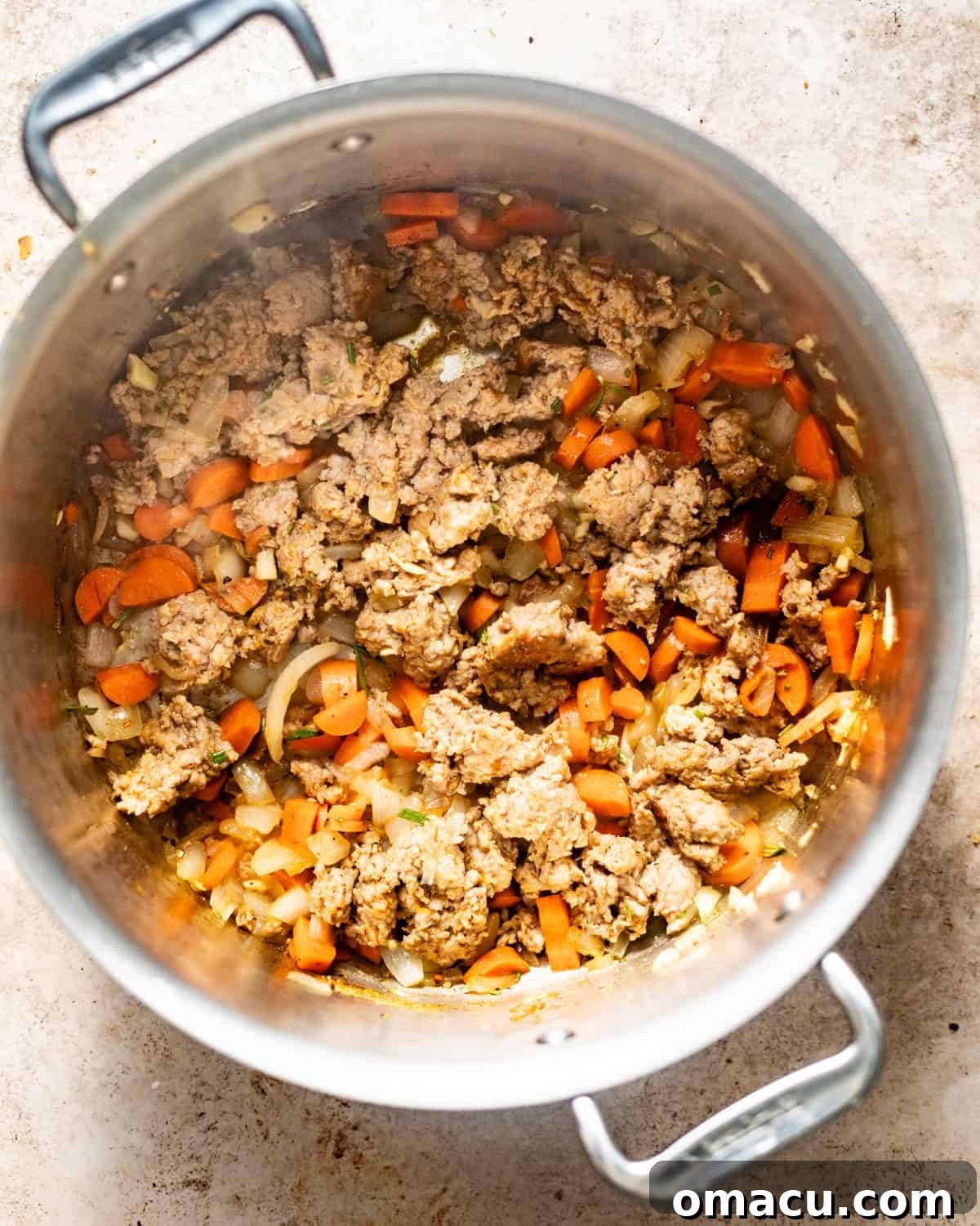 Ground Italian sausage and diced vegetables (white onion, celery) sizzling and beginning to brown in a large pot or Dutch oven.