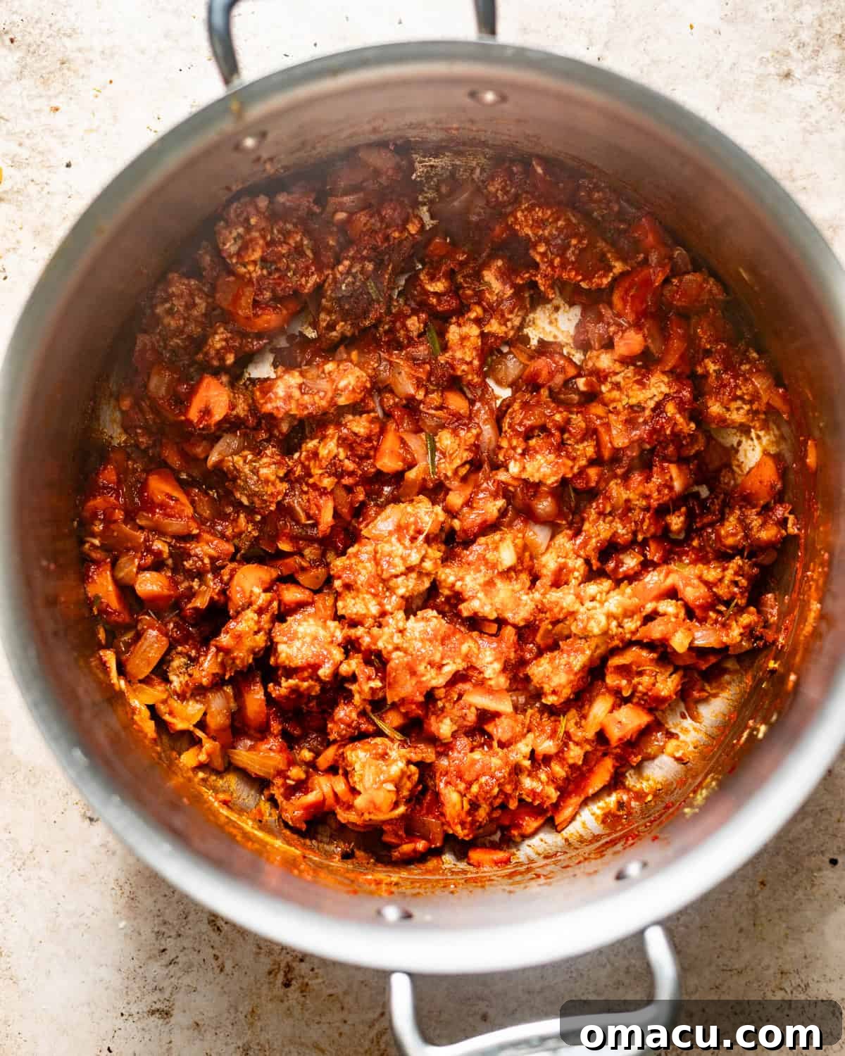 Sautéed ground sausage, softened vegetables, and a rich dollop of red tomato paste, blended with aromatic herbs, in a large pot, creating a deep flavor base.