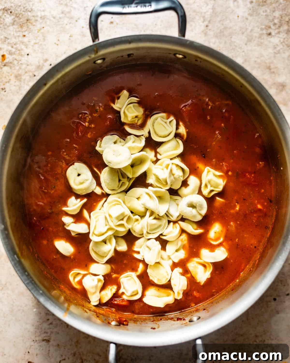 The Tuscan soup simmering gently in a large pot with tender cheese tortellini just added, absorbing the delicious broth and flavors.