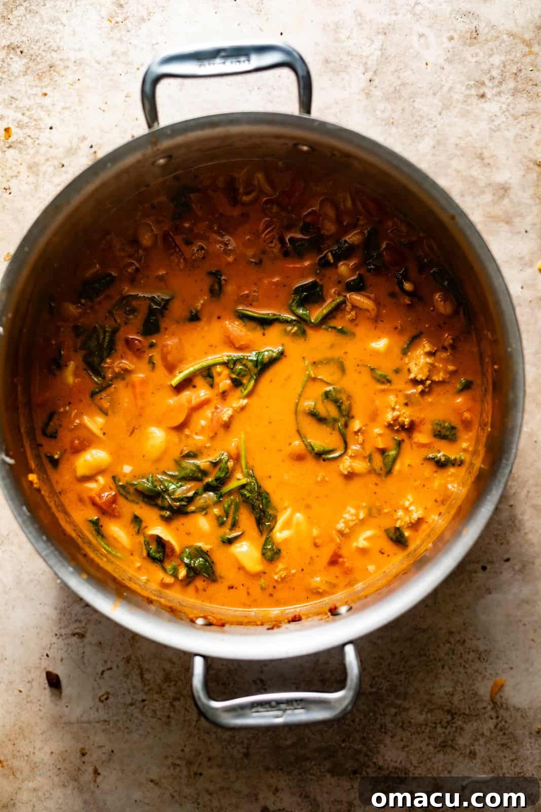 The final stage of Tuscan soup preparation, with vibrant fresh spinach and creamy cannellini beans stirred into the rich, thickened broth.