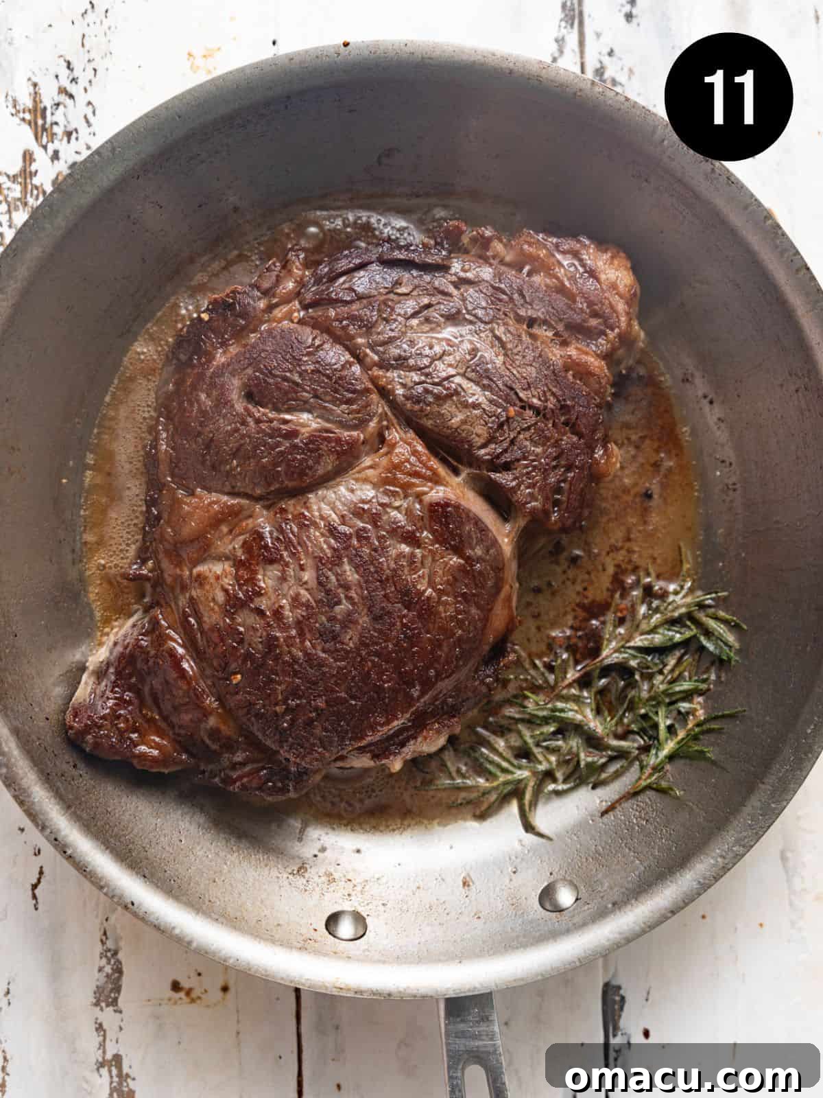 Perfectly seared ribeye steak in a skillet, surrounded by melted butter, fresh garlic cloves, and aromatic rosemary sprigs for basting.
