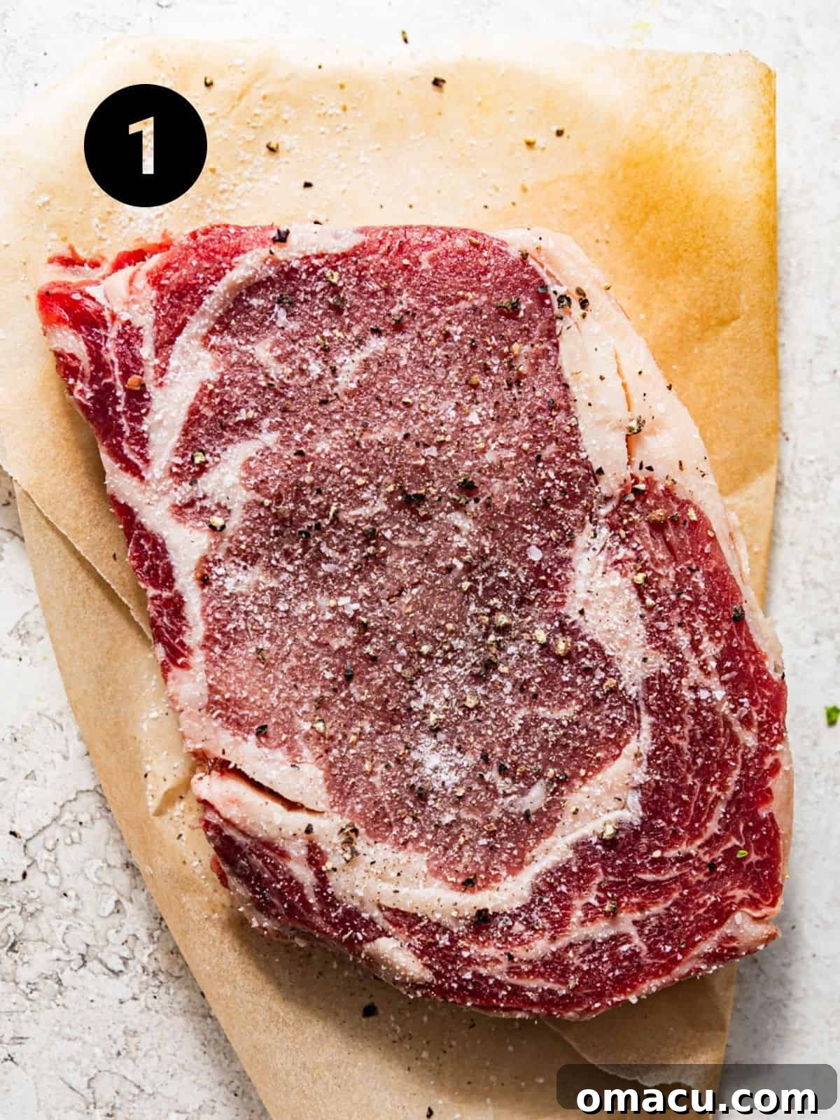 Seasoned ribeye steak on a piece of parchment paper, ready for cooking.