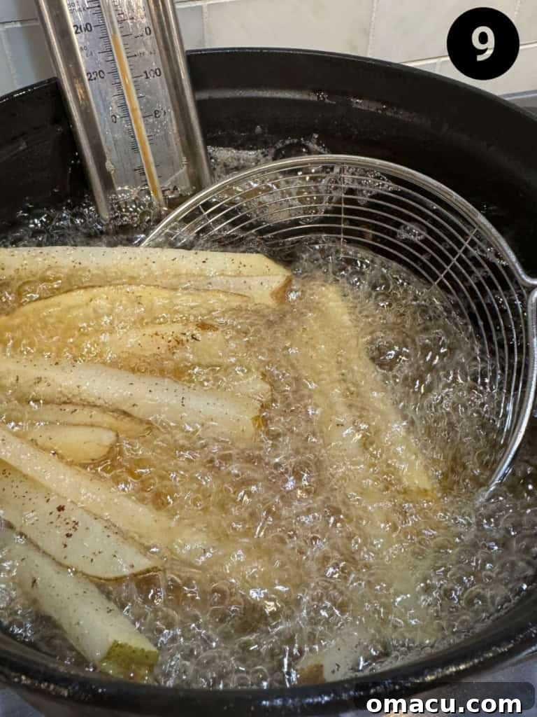 French fries being fried in a pot of hot vegetable oil during the first fry.