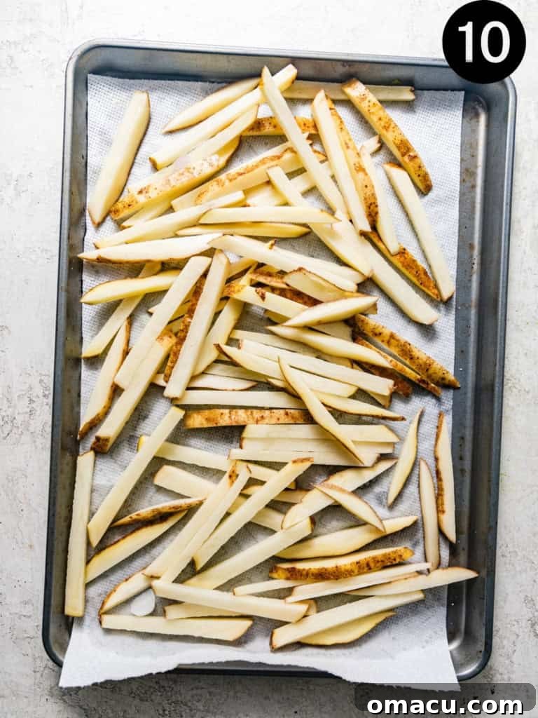 Golden-brown, crispy French fries piled on a baking sheet lined with paper towels to drain after the second fry.