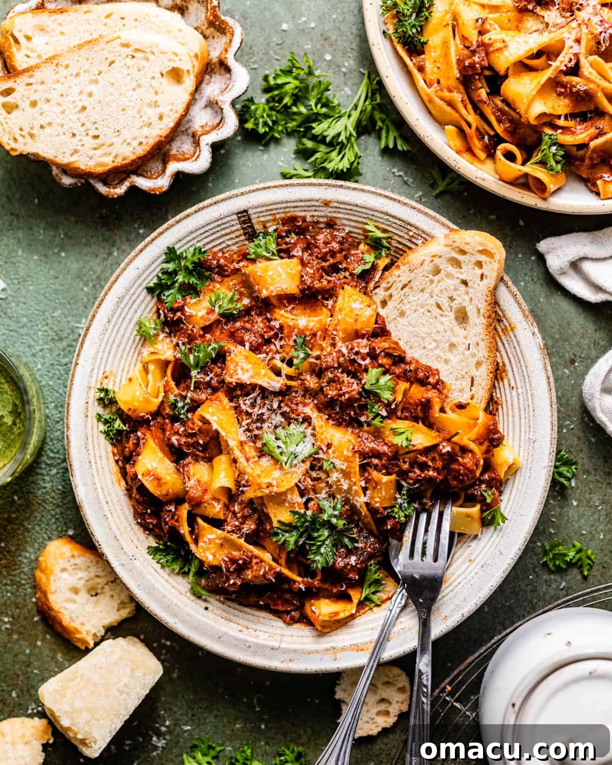 A generous serving of short rib bolognese pasta in a white bowl, garnished with fresh parsley and grated parmesan, accompanied by crusty bread and a fork.