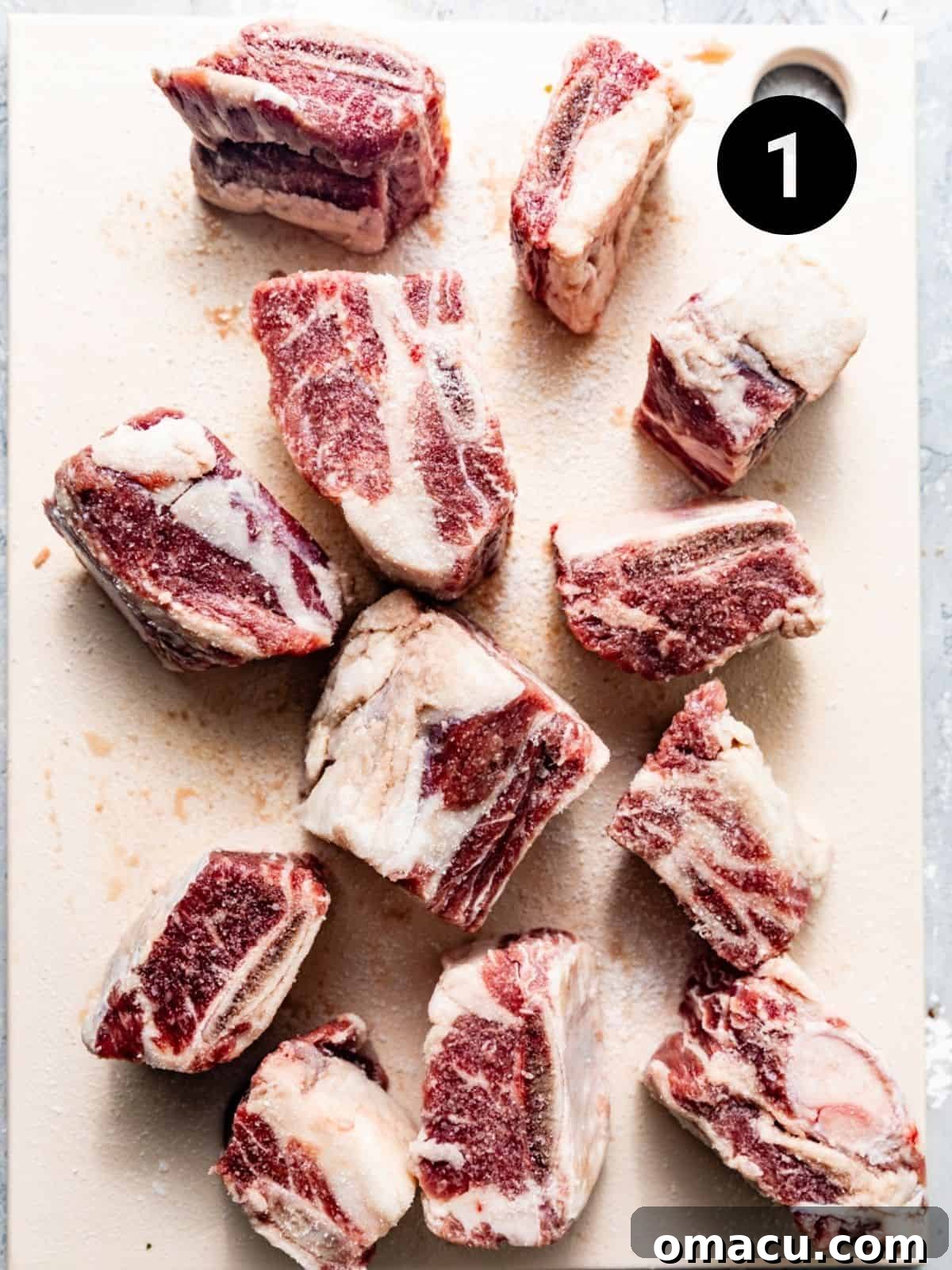Beef short ribs seasoned generously with kosher salt and black pepper on a wooden cutting board.
