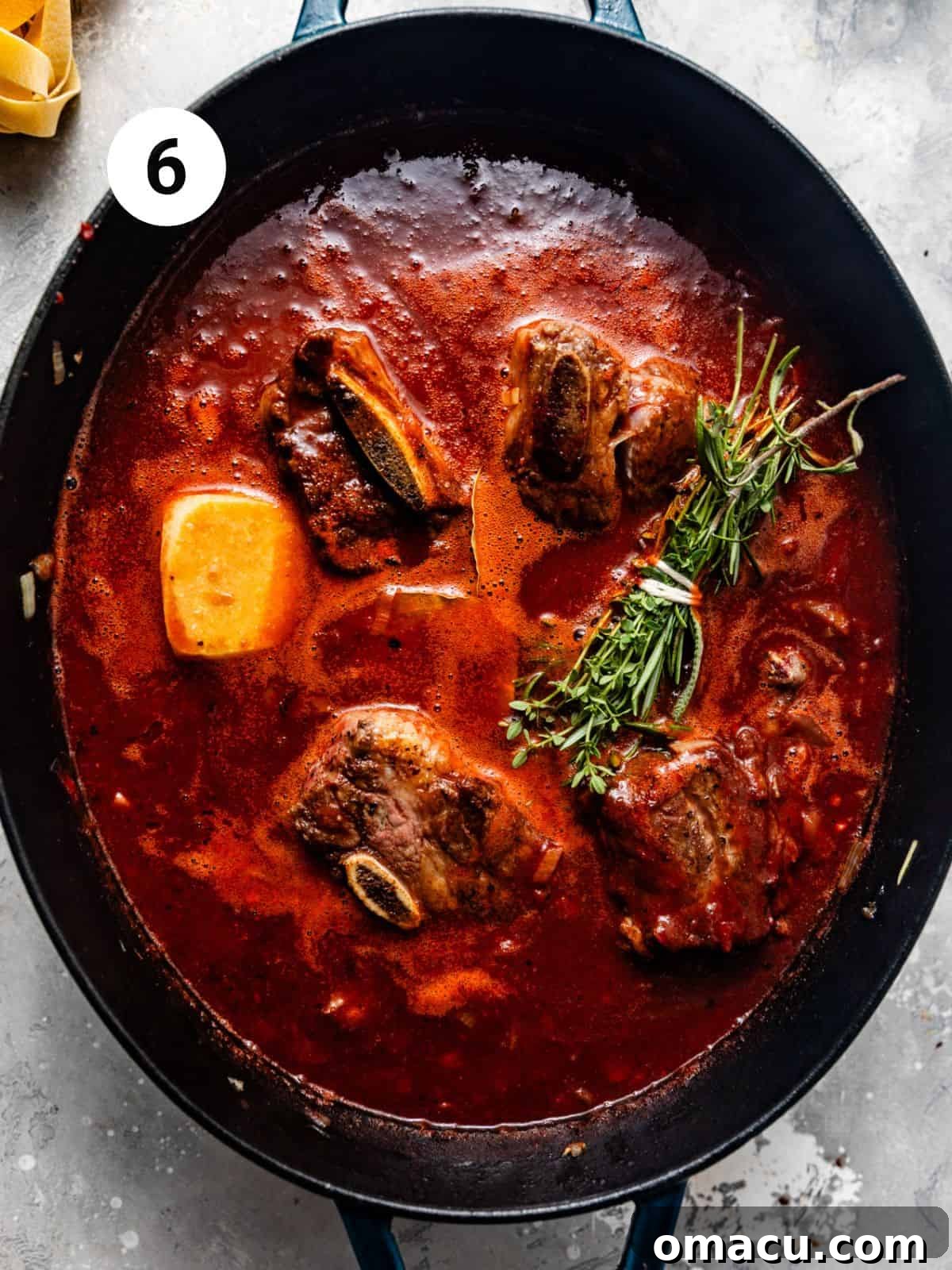Close-up of short ribs, fresh herbs, and a parmesan rind simmering in a large pot of rich tomato and wine sauce.